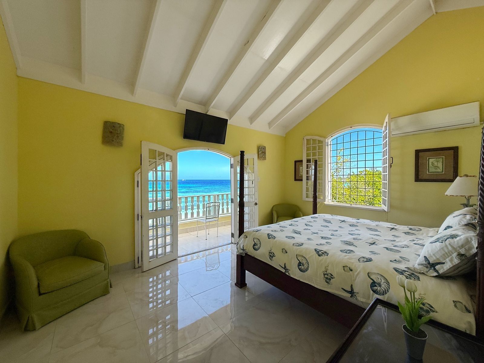 A bedroom with a four-poster bed and open doors to a balcony with a sea view.