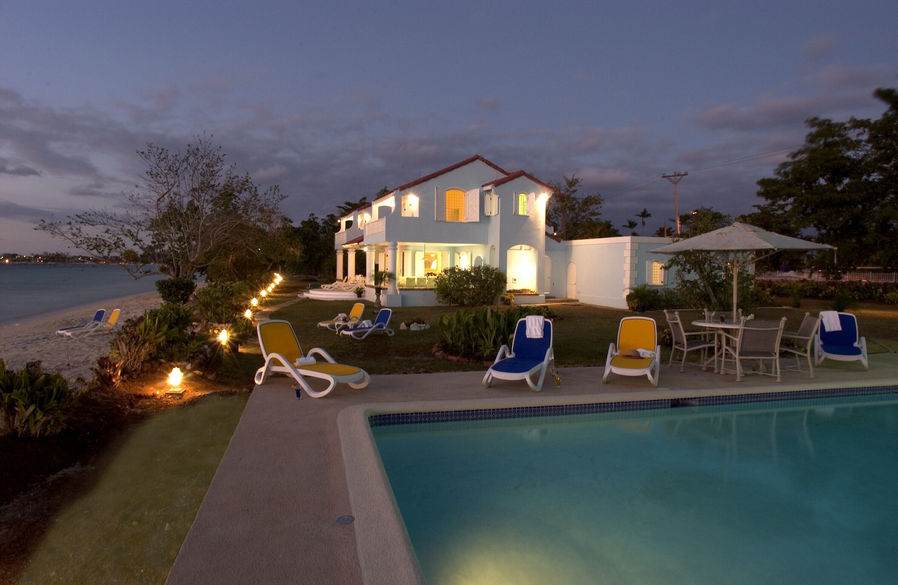 The villa and the pool at dusk with the lights on.