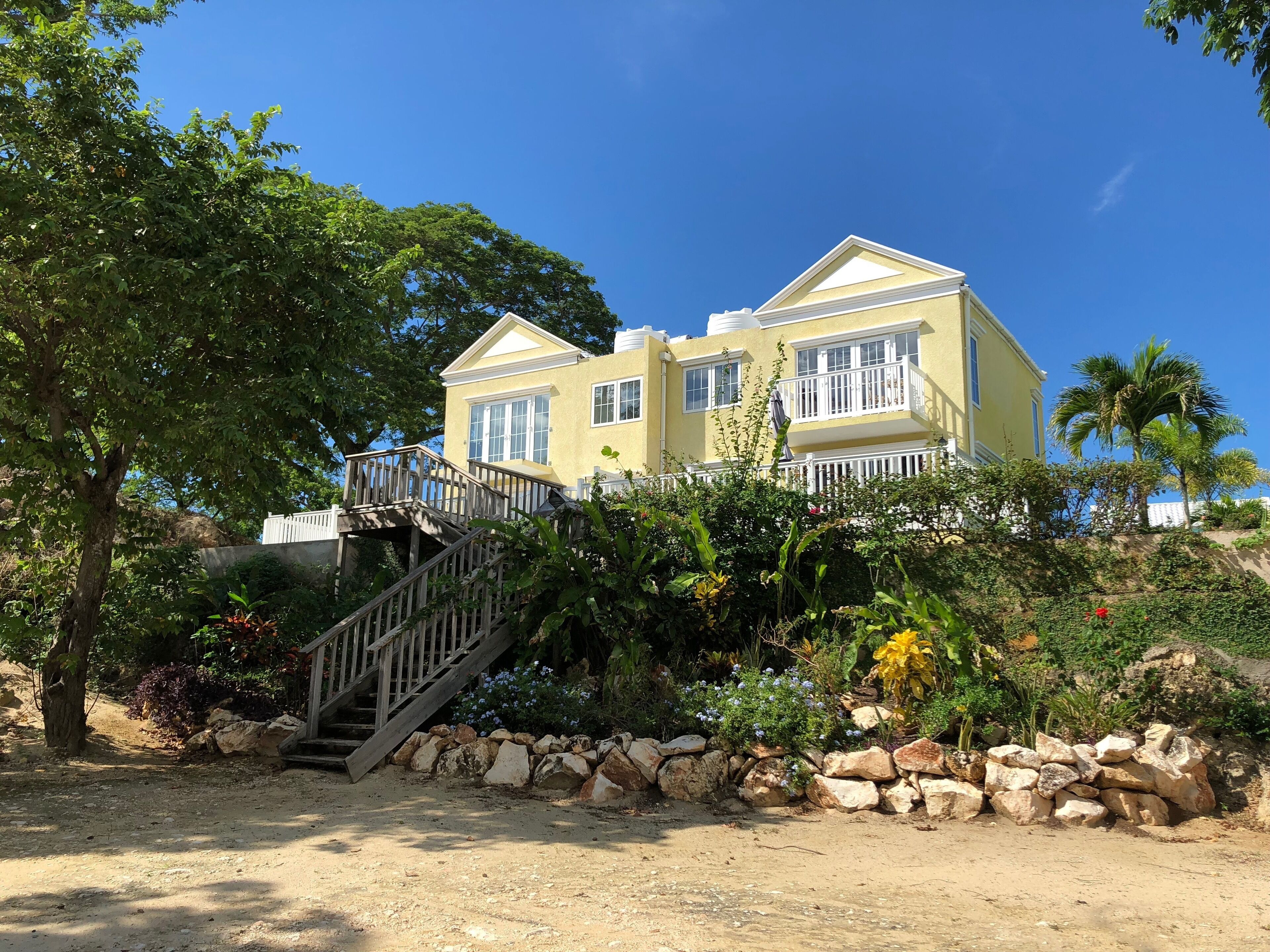 A yellow two-story townhome stands above a garden with wooden stairs.