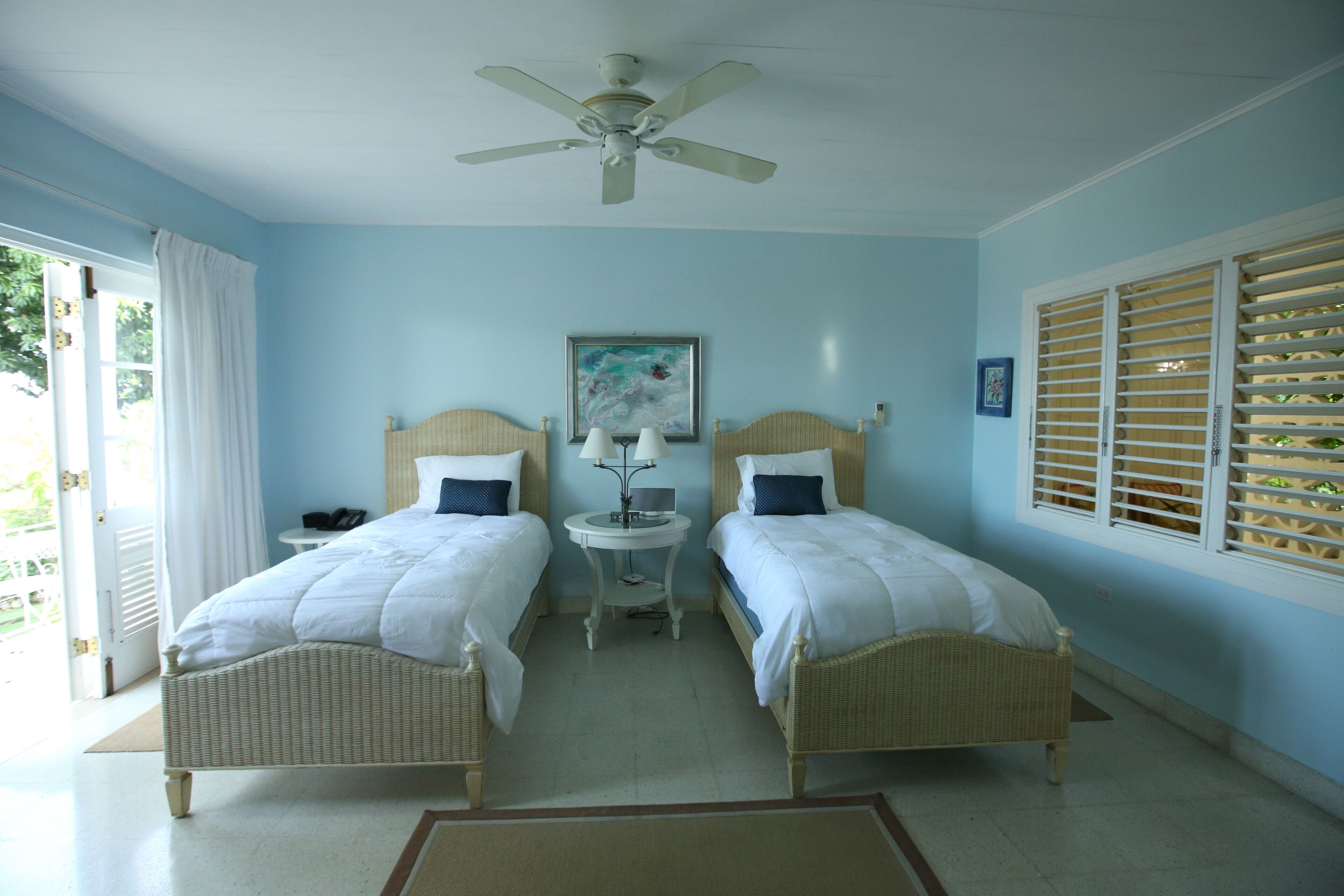 A bedroom with two single beds, light blue walls, and a ceiling fan.