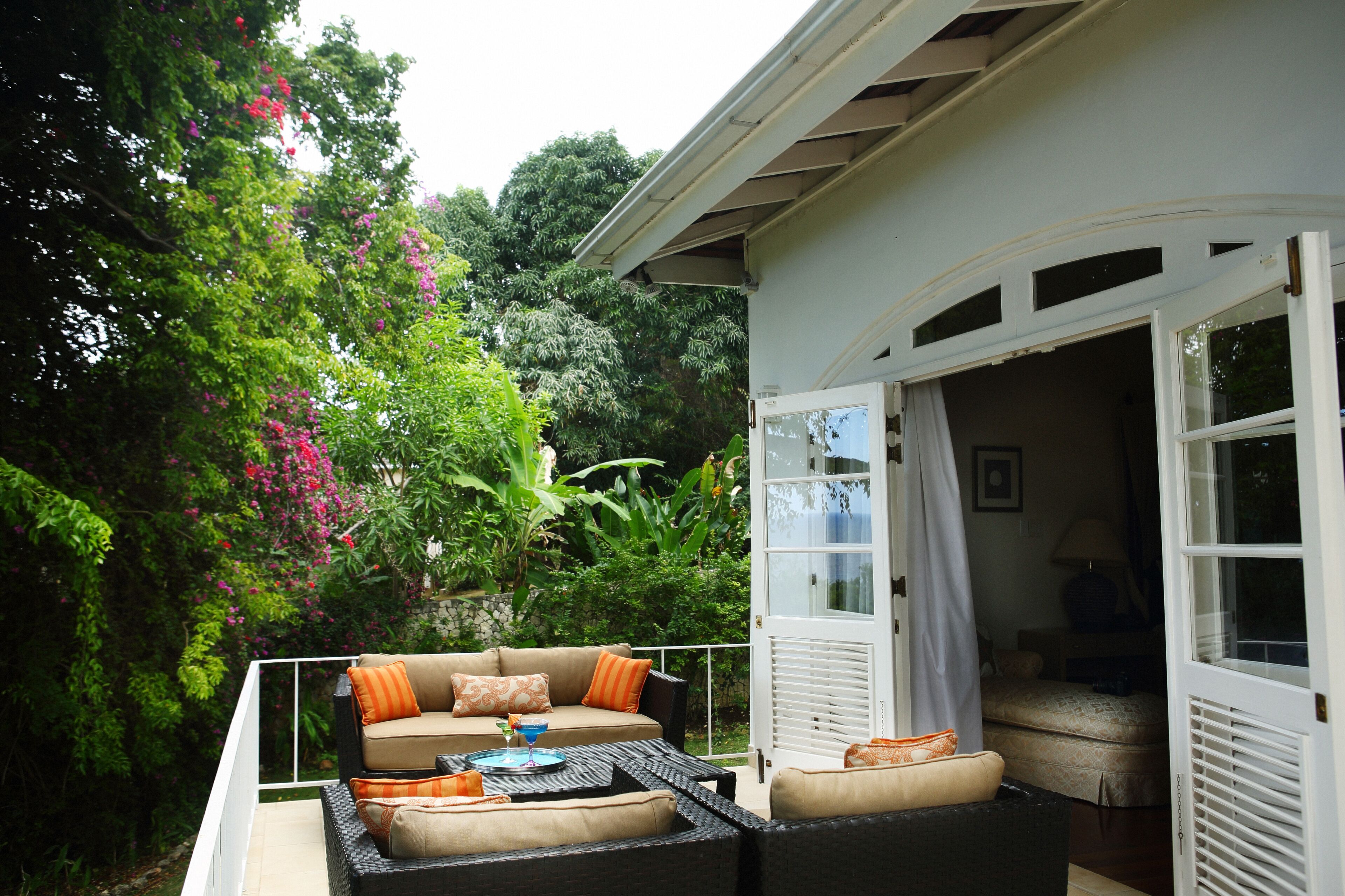 A terrace with wicker seats and orange pillows outside a bedroom.
