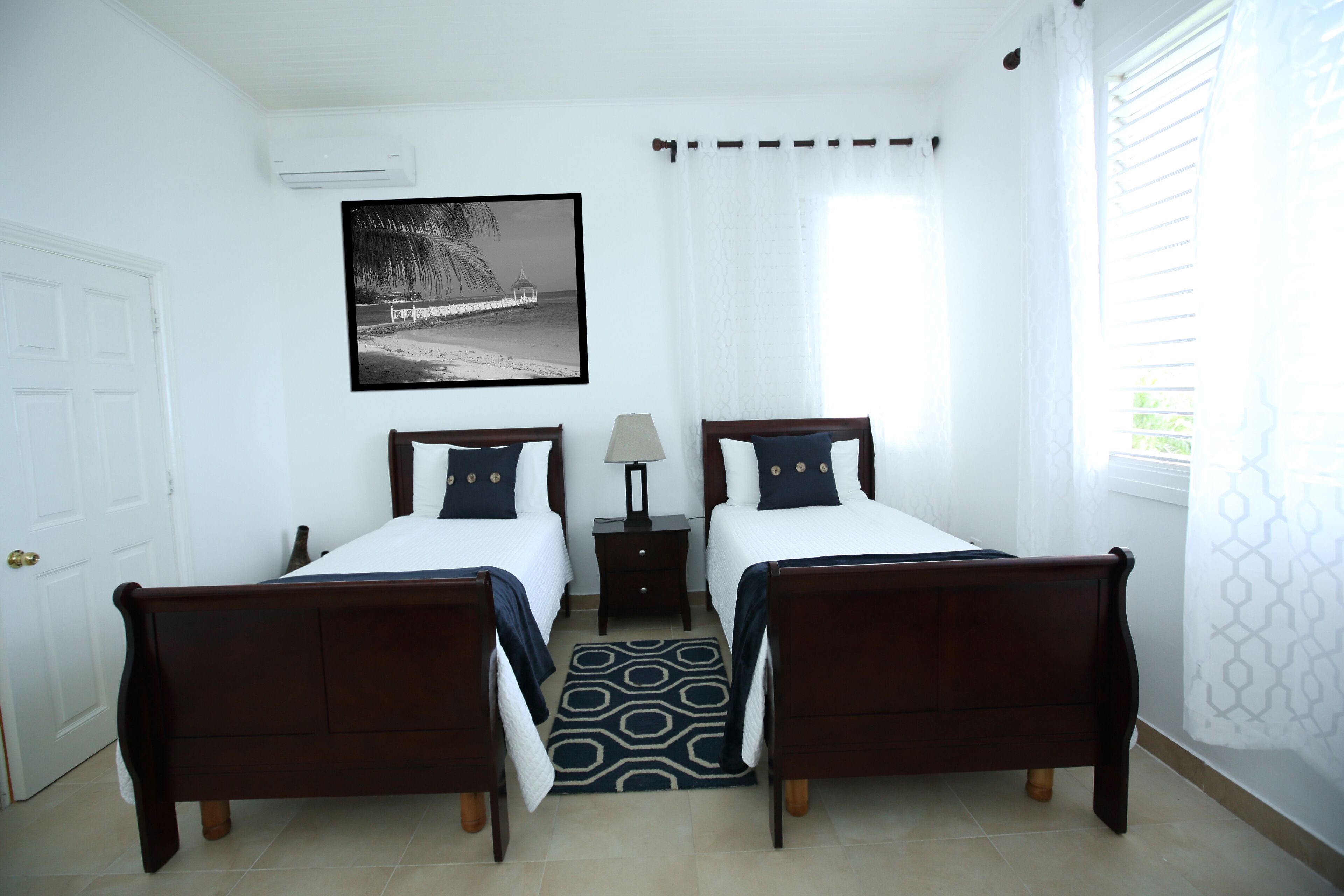 A bedroom with two single beds, white walls, and a picture of a beach.