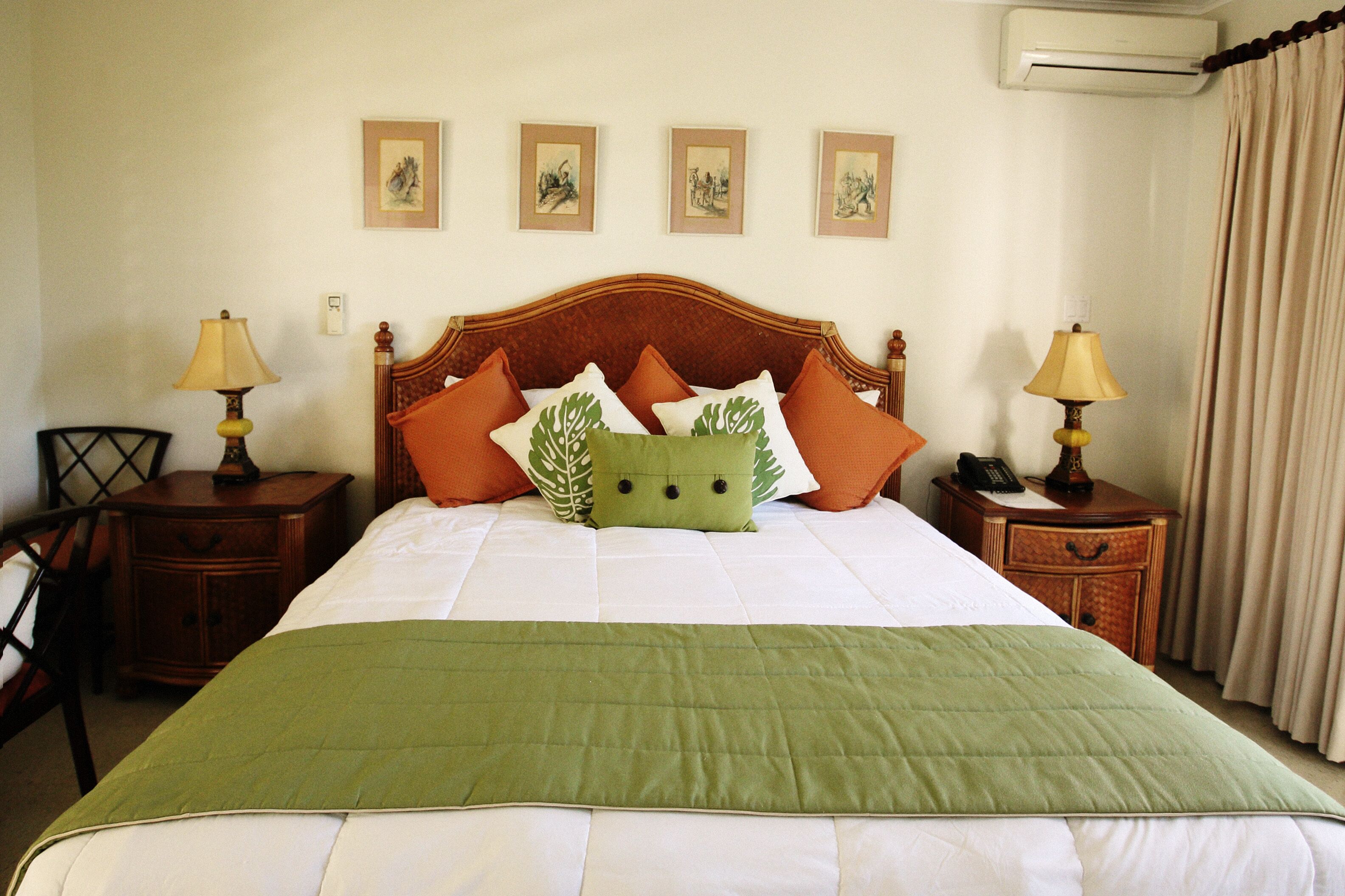 A bedroom with a large bed, a rattan headboard, and orange and green pillows.
