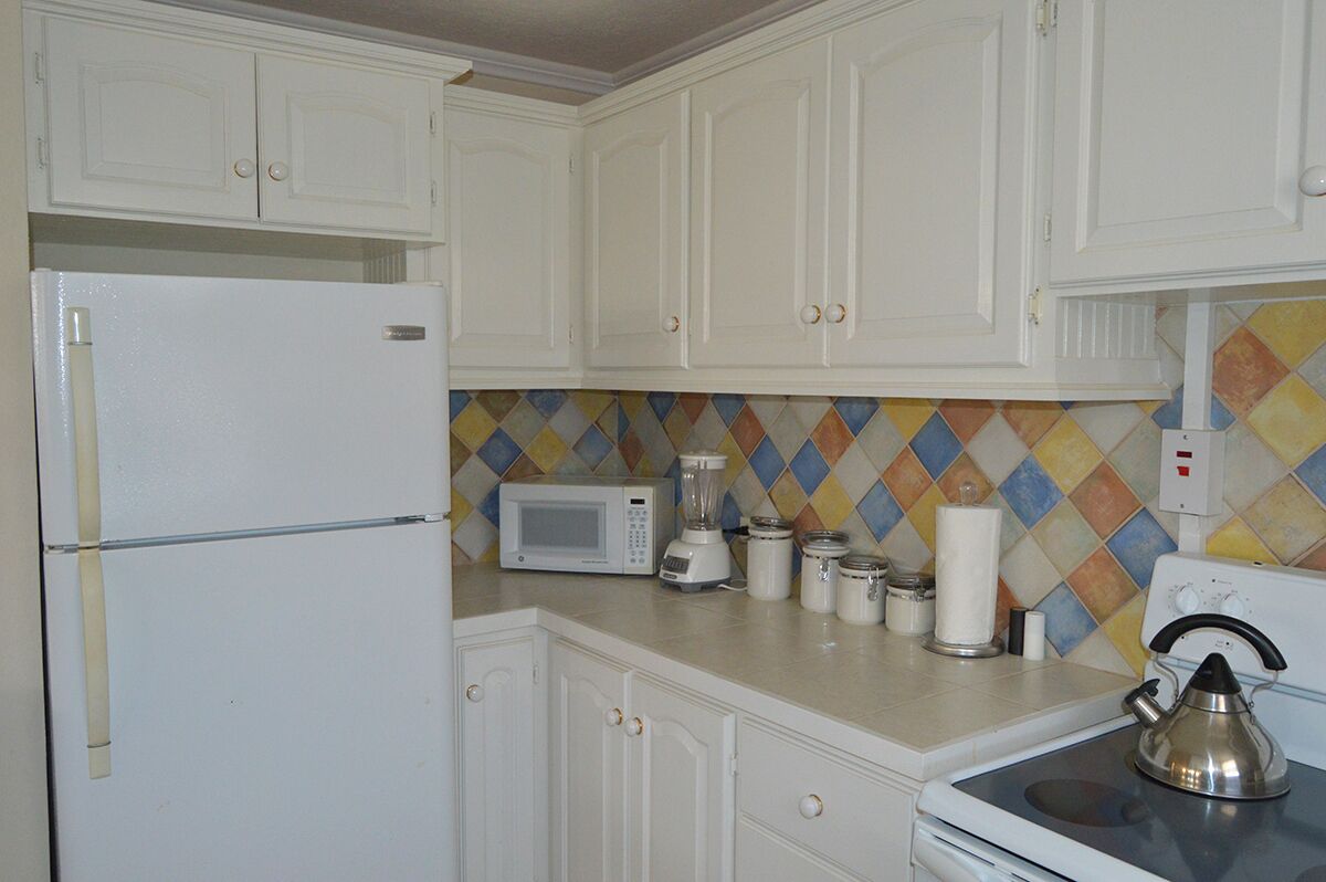 The kitchen with a refrigerator, a microwave oven, and tiled walls.