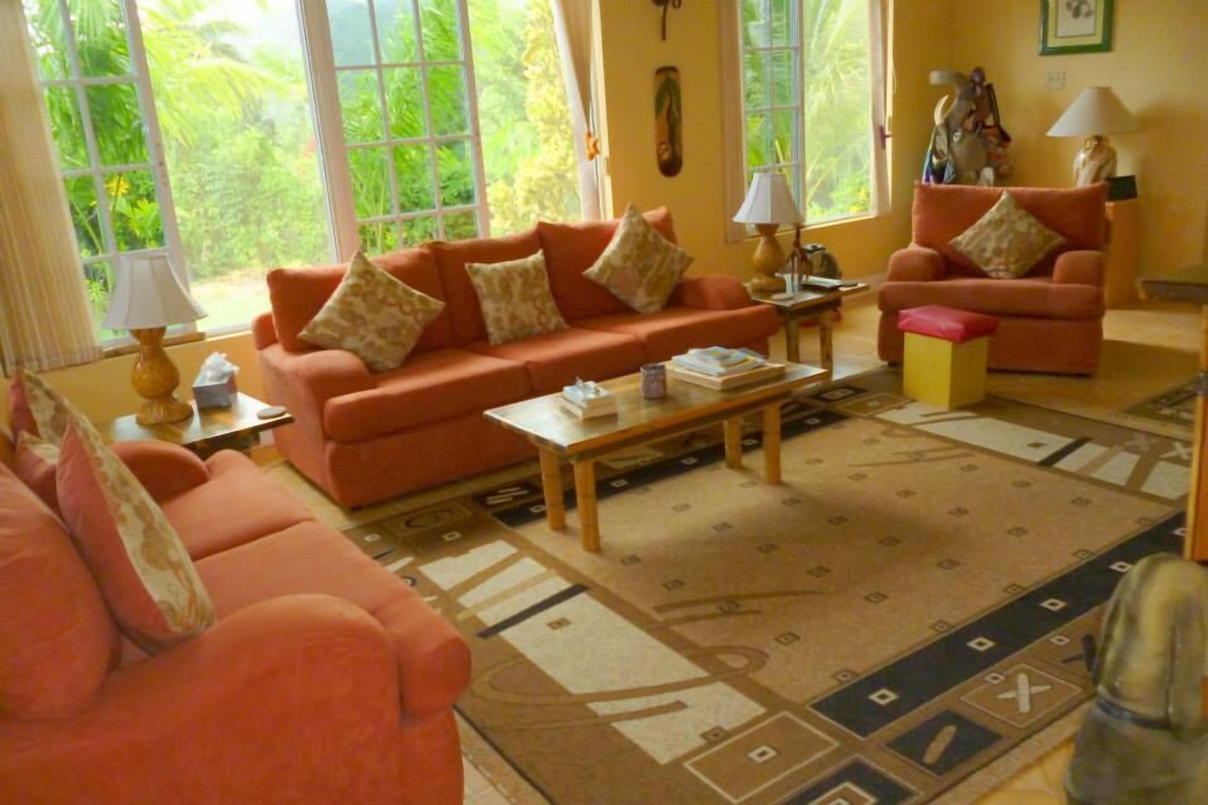 A living room with orange sofas, a coffee table, and large windows.