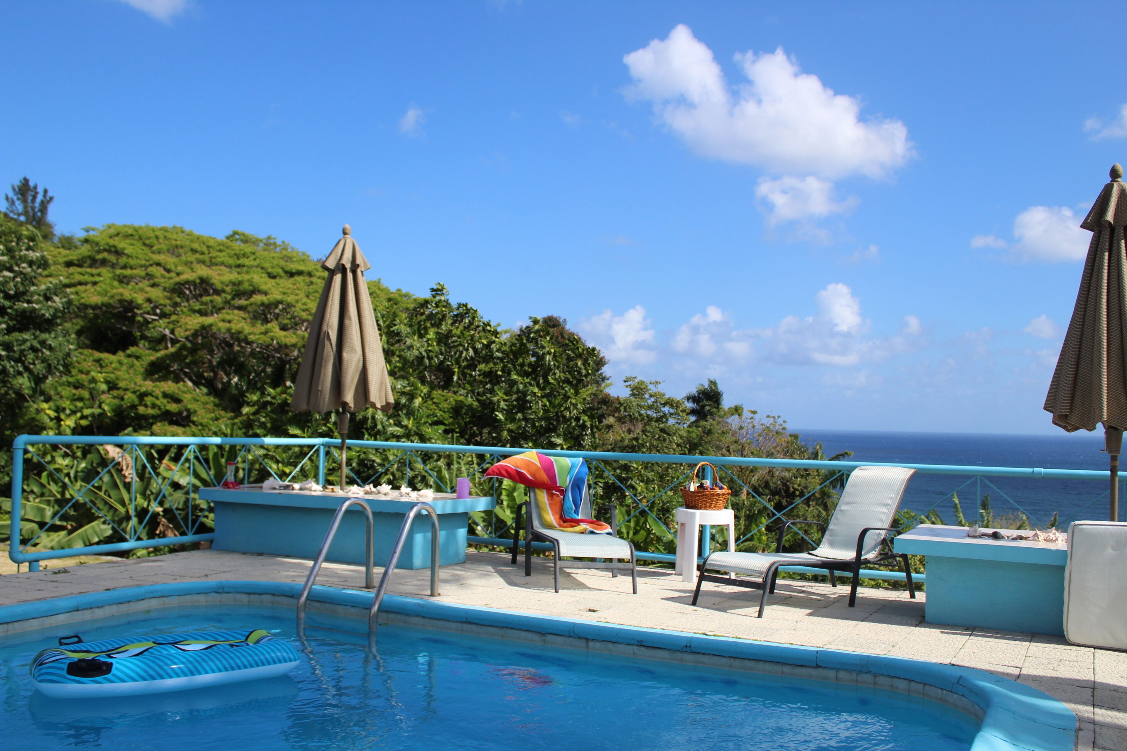 The pool with a float, lounge chairs, and a view of the sea.