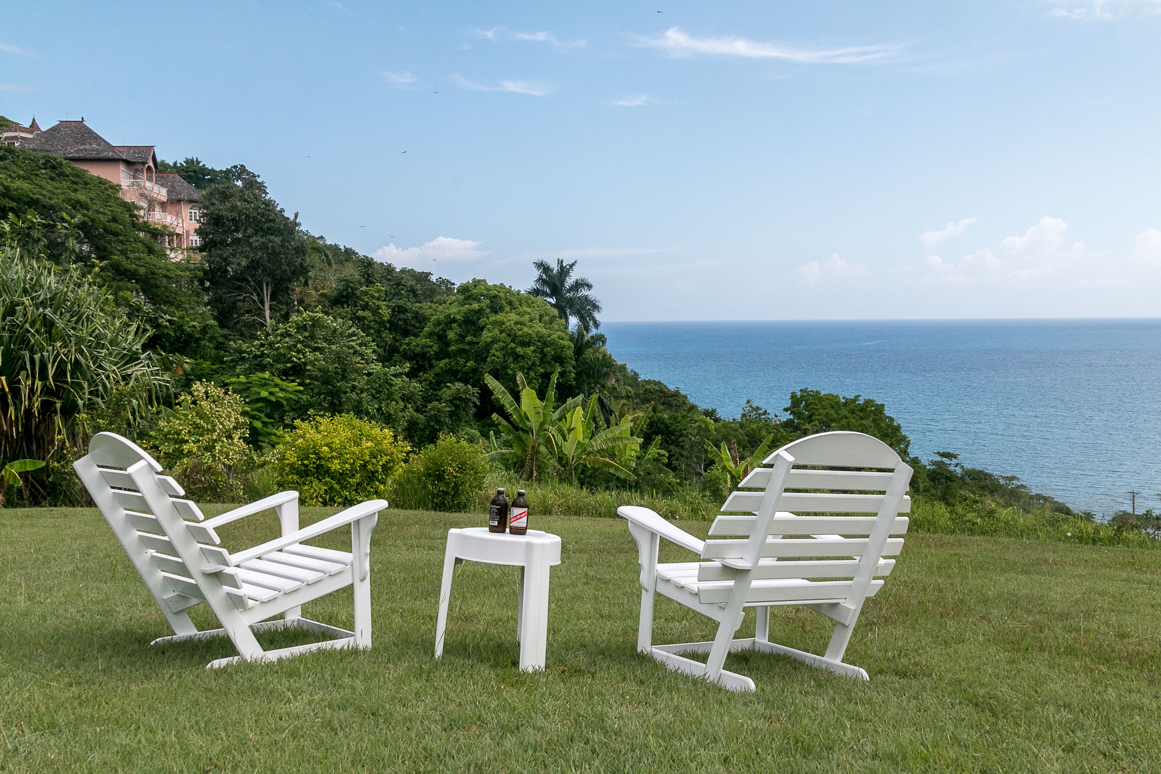 Two white chairs and a small table on the lawn above the sea.