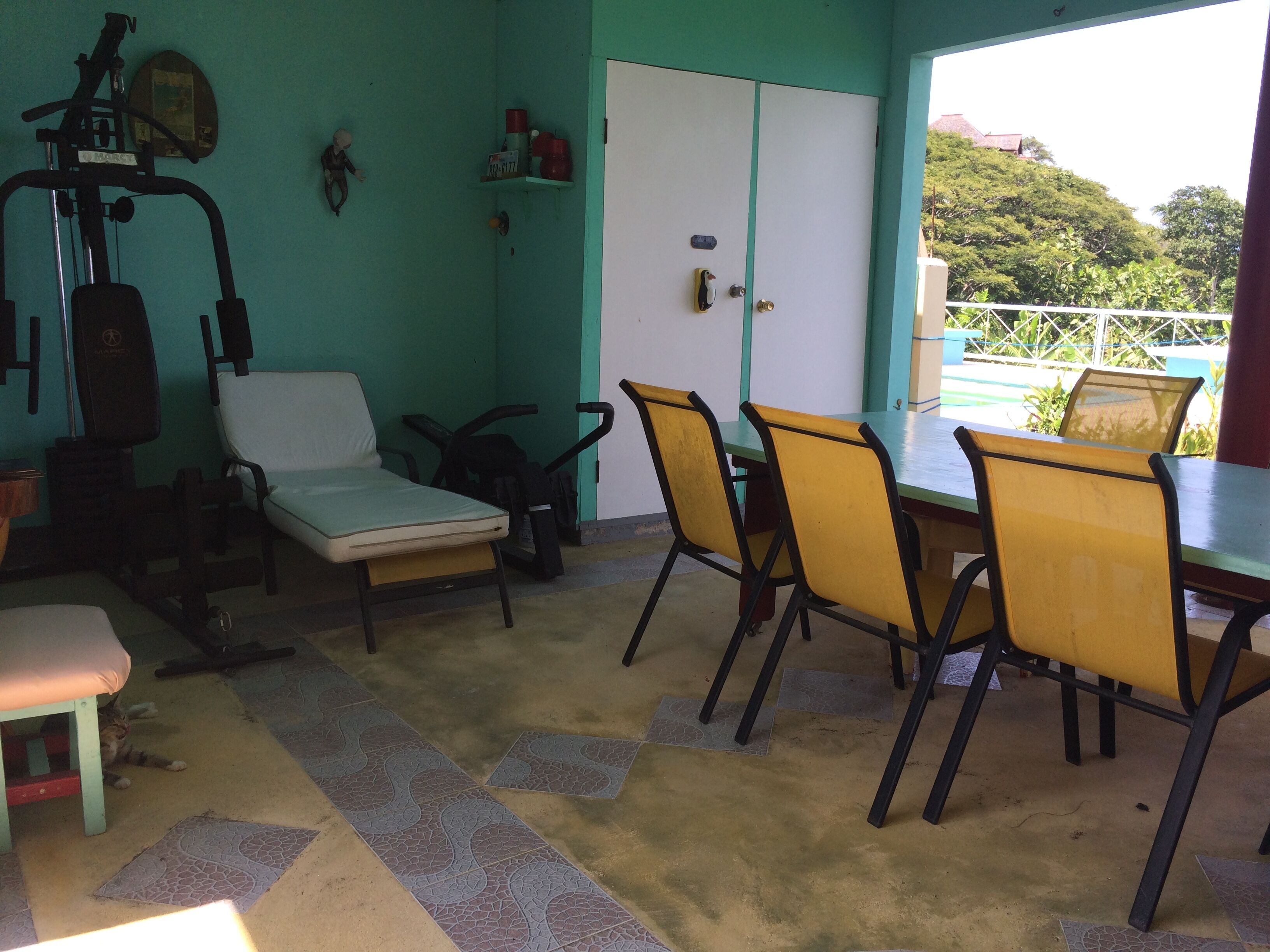 A covered patio with a dining table, chairs, and exercise equipment.