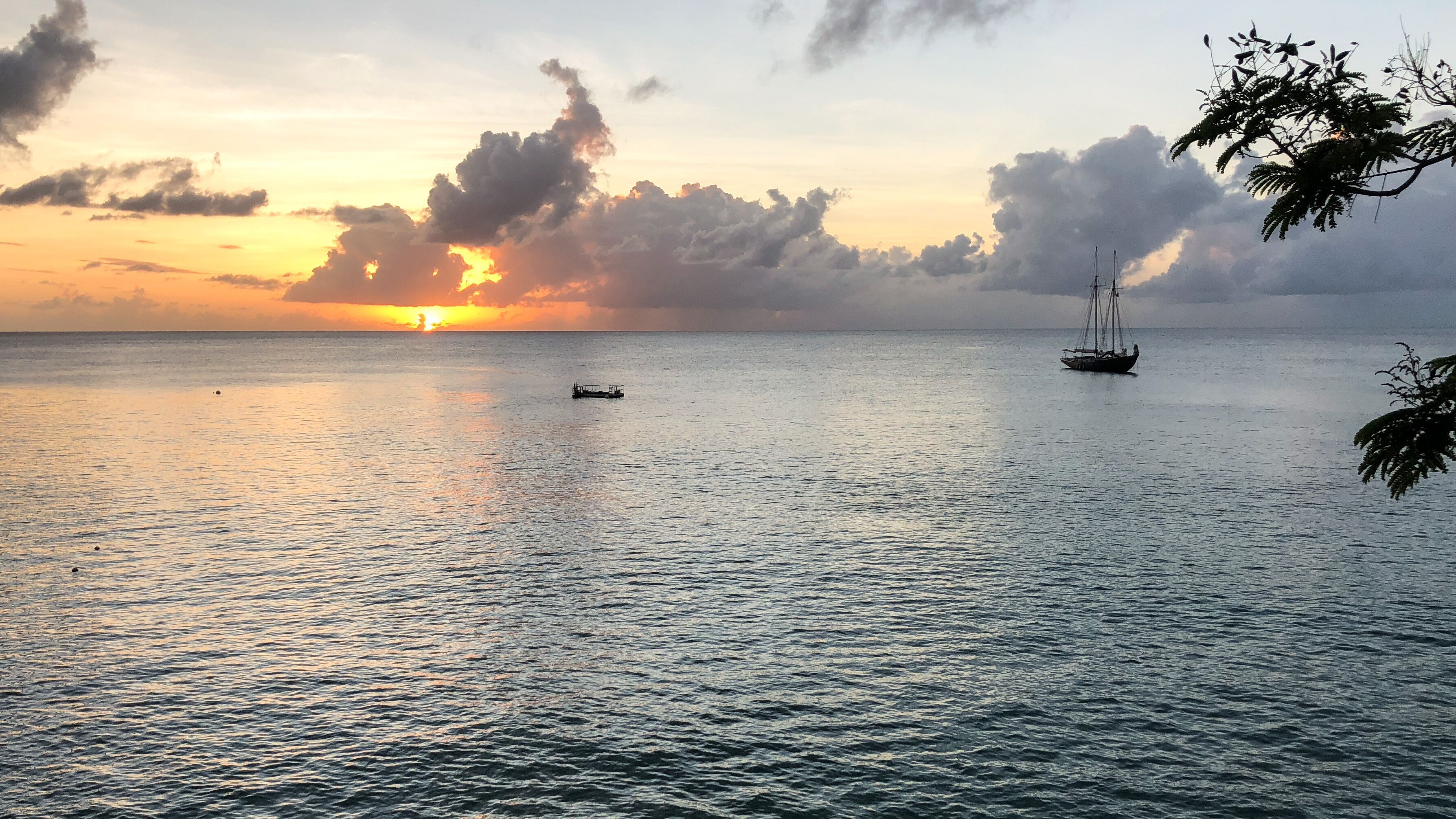 A sunset over the sea with a sailboat at anchor.