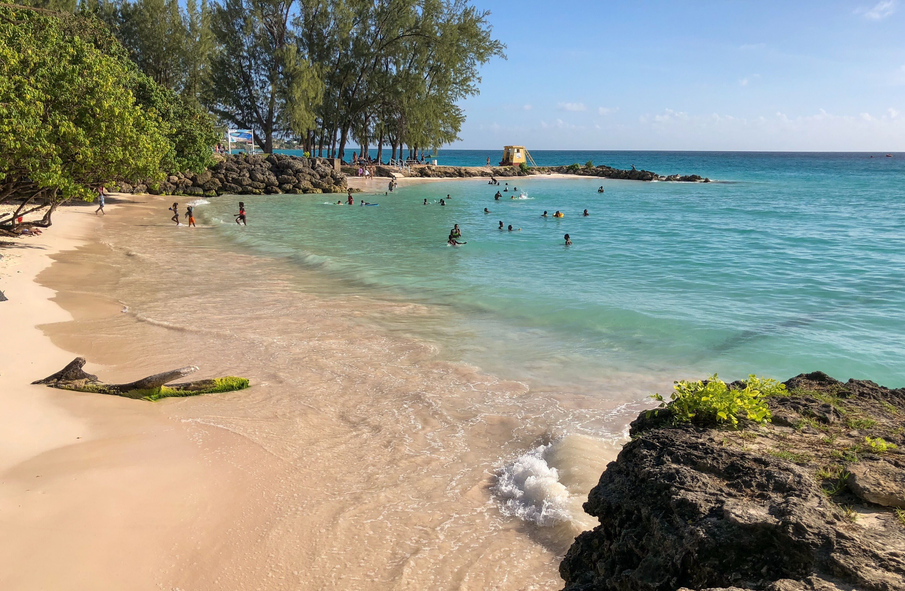 A sand beach with swimmers in a shallow bay.