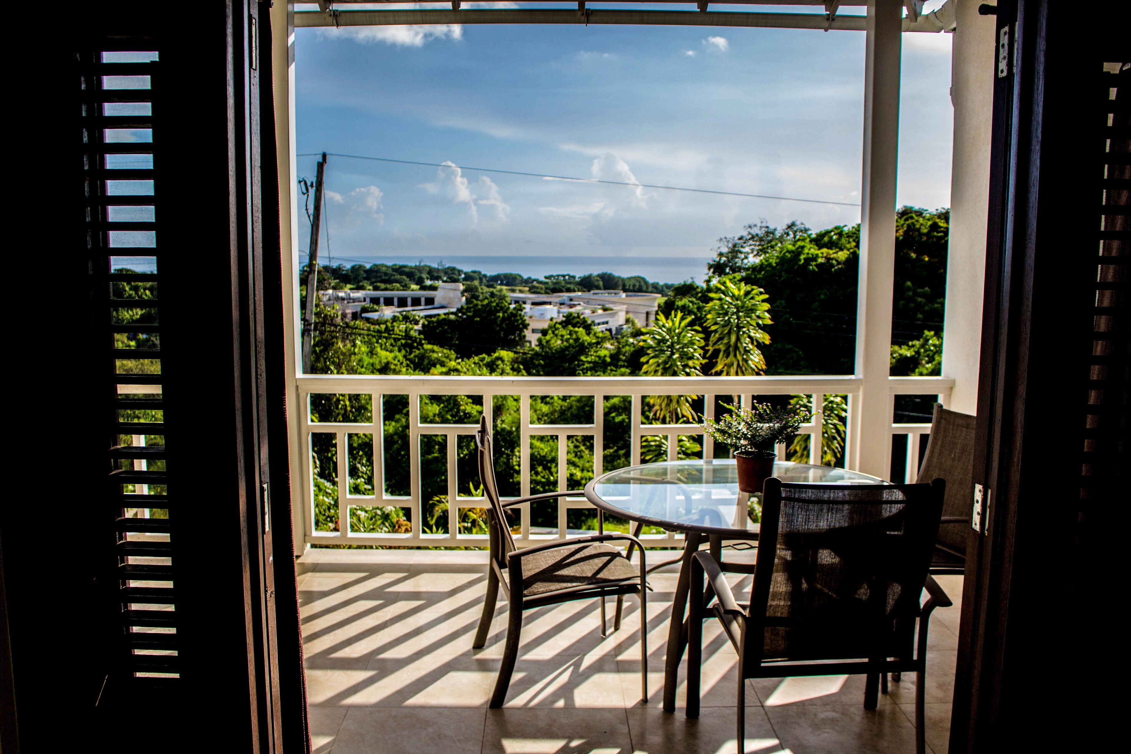 A balcony with a table, chairs, and a view of trees and the sea.