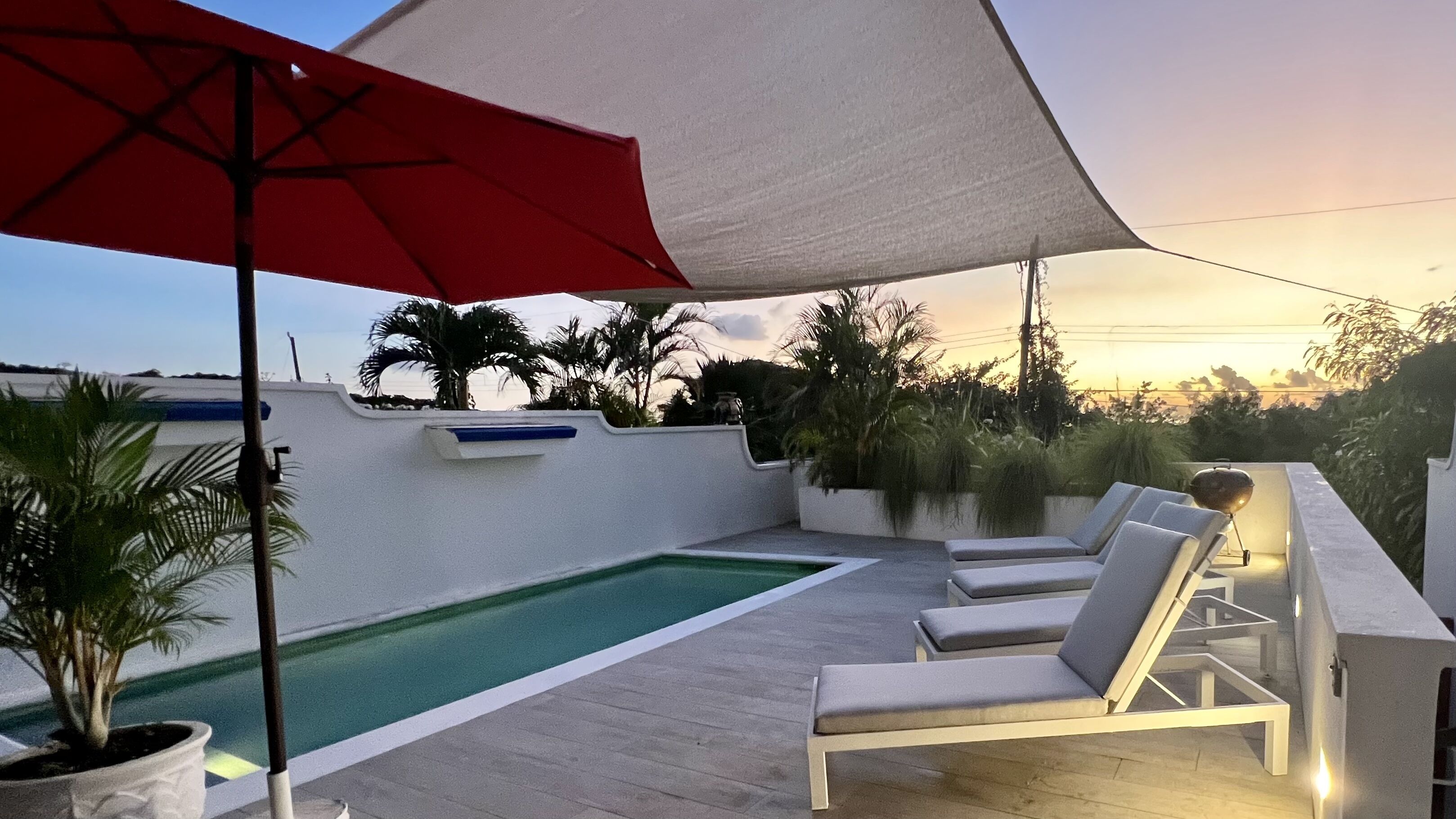 A pool terrace with sun loungers and an umbrella at dusk.