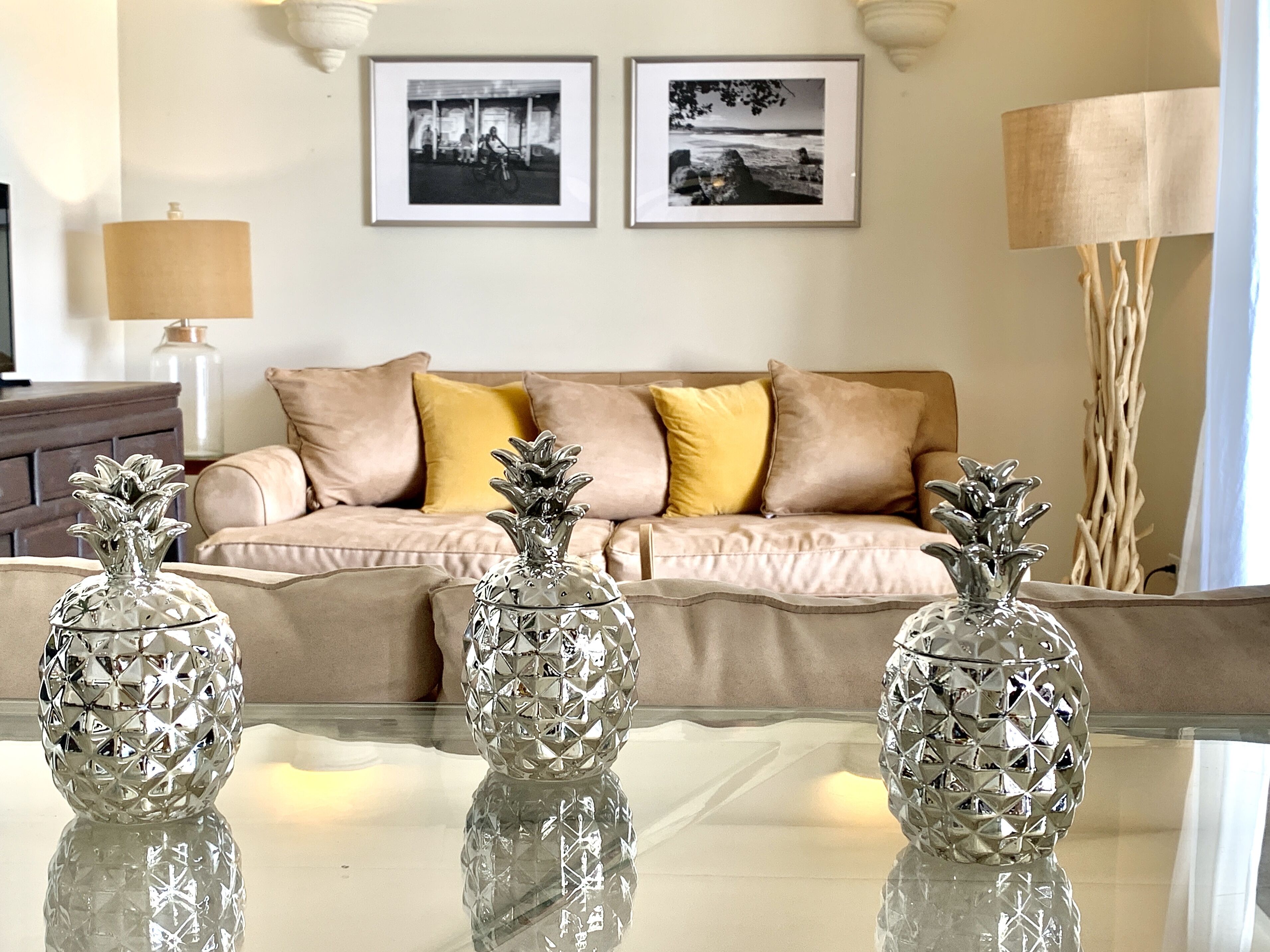 Three silver pineapple ornaments on a glass table in front of a sofa.