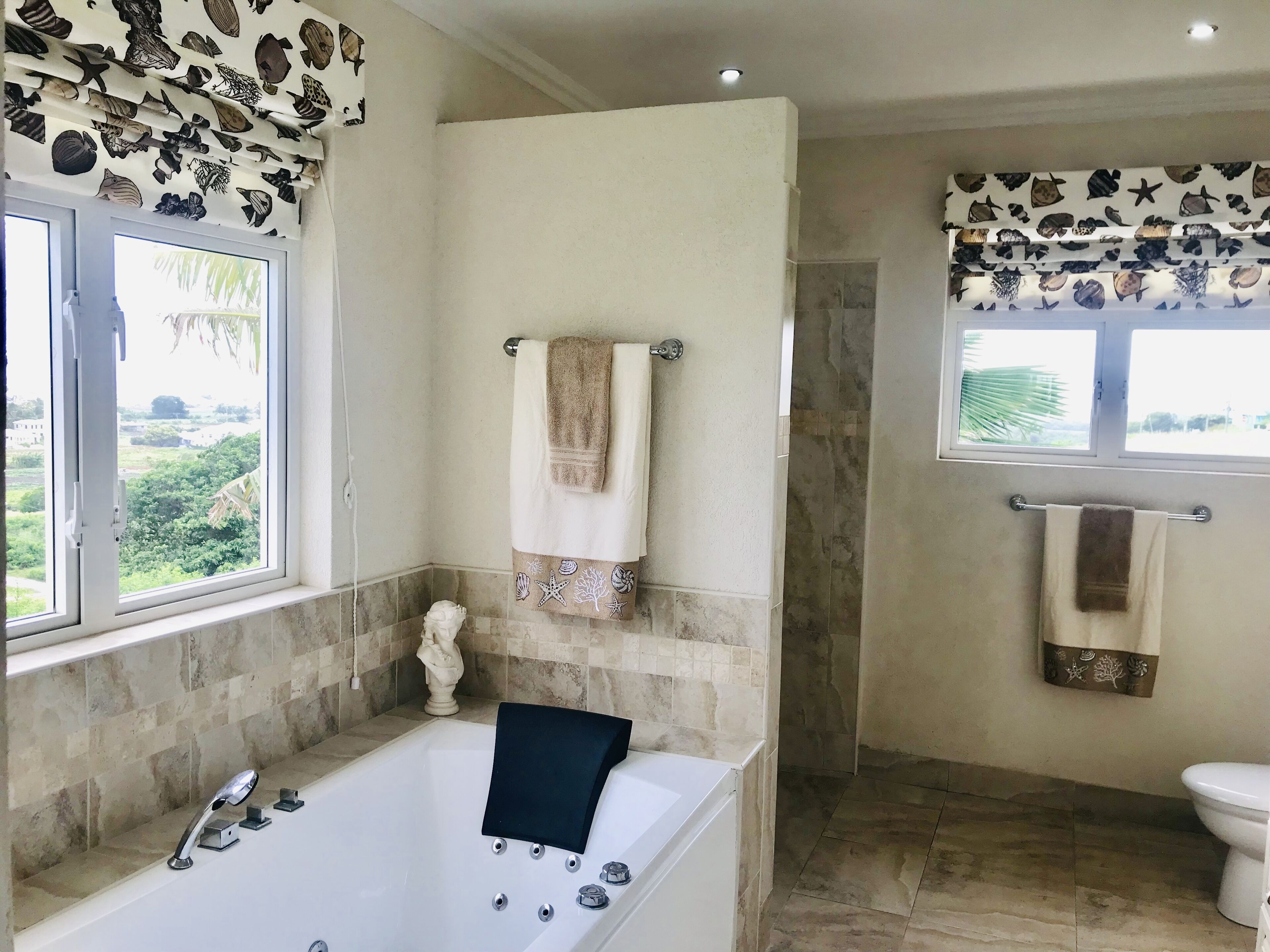 A bathroom with a bath tub, two windows, and towels on rails.