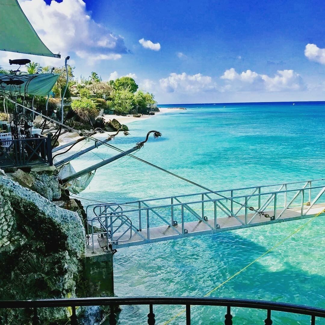 A metal walkway over clear water next to a rocky shore.