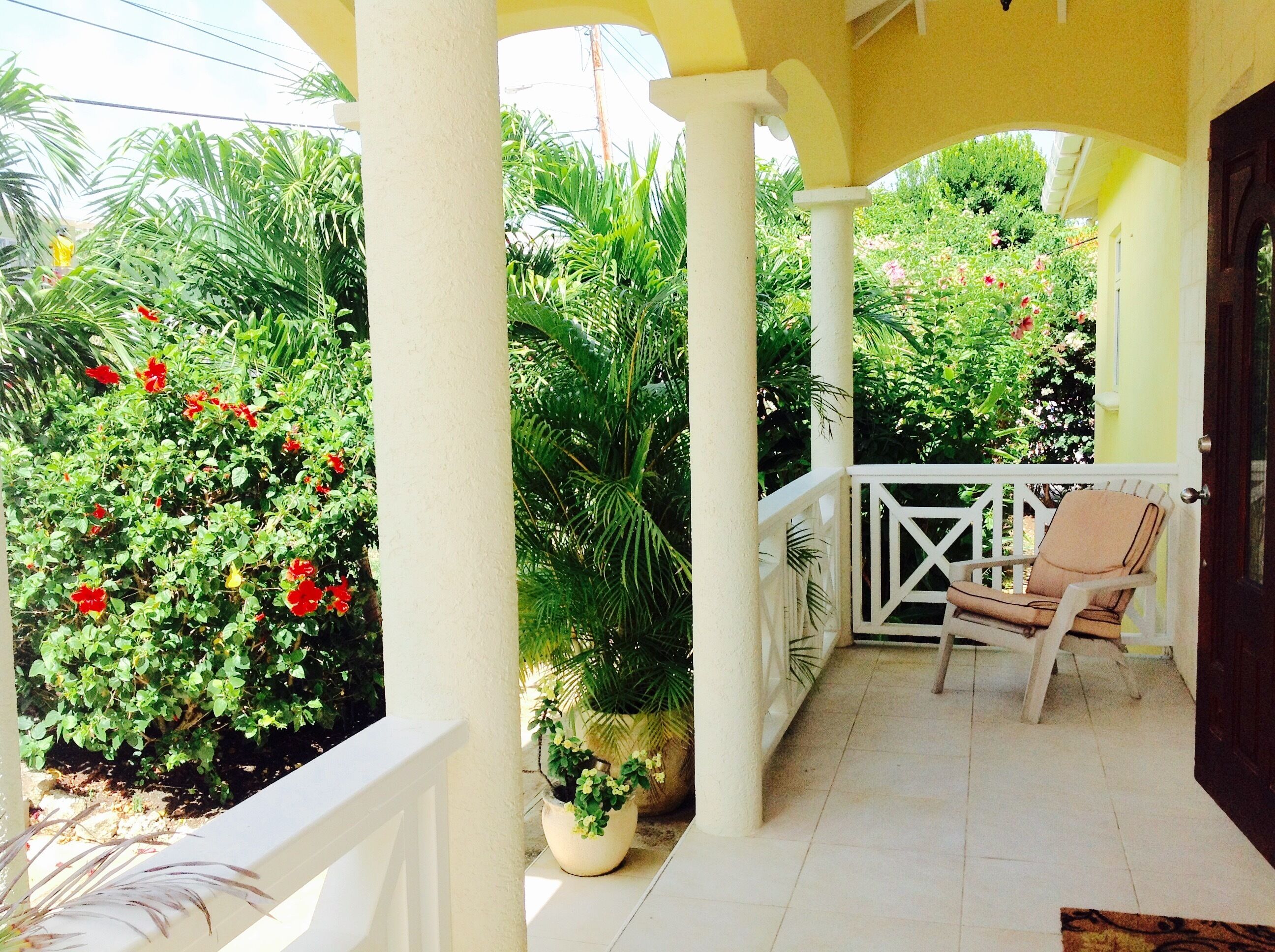 A covered porch with columns, a chair, and flower bushes.
