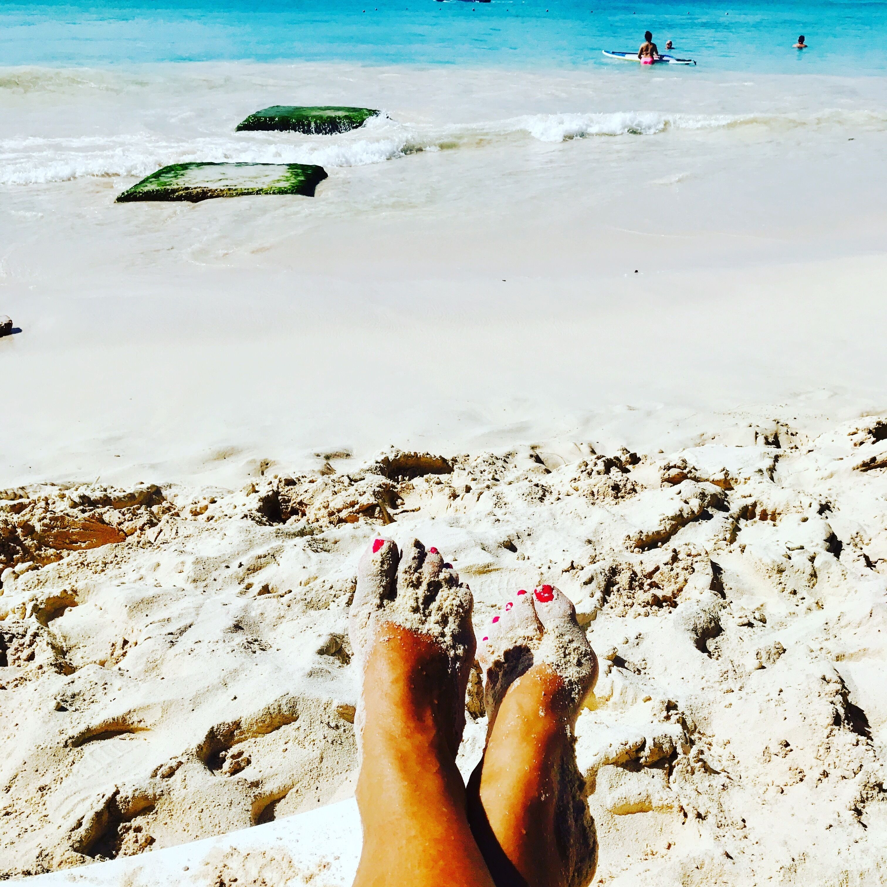 A view of the beach and swimmers from a sun lounger.