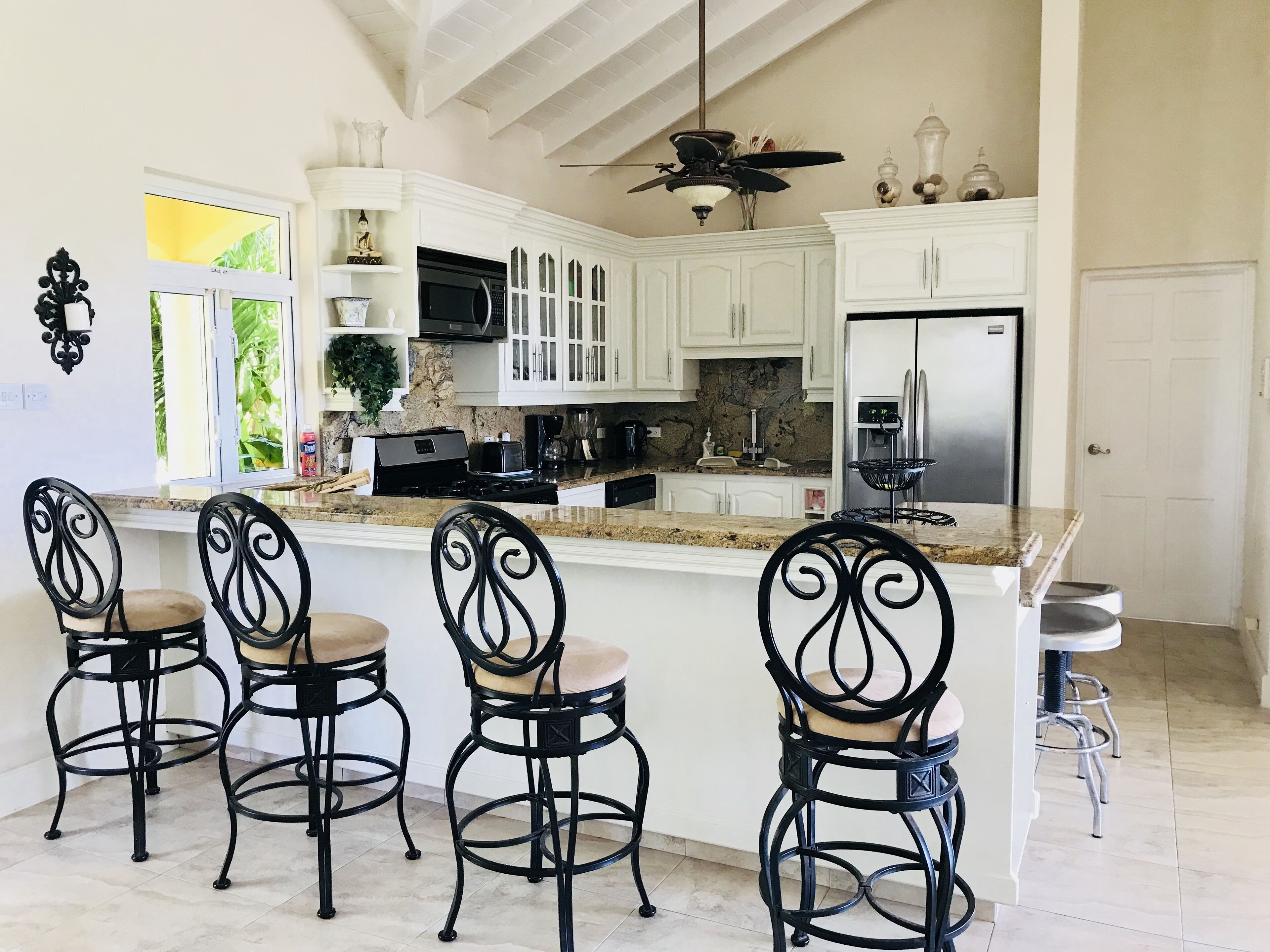 A kitchen with white cabinets and a breakfast bar with four stools.