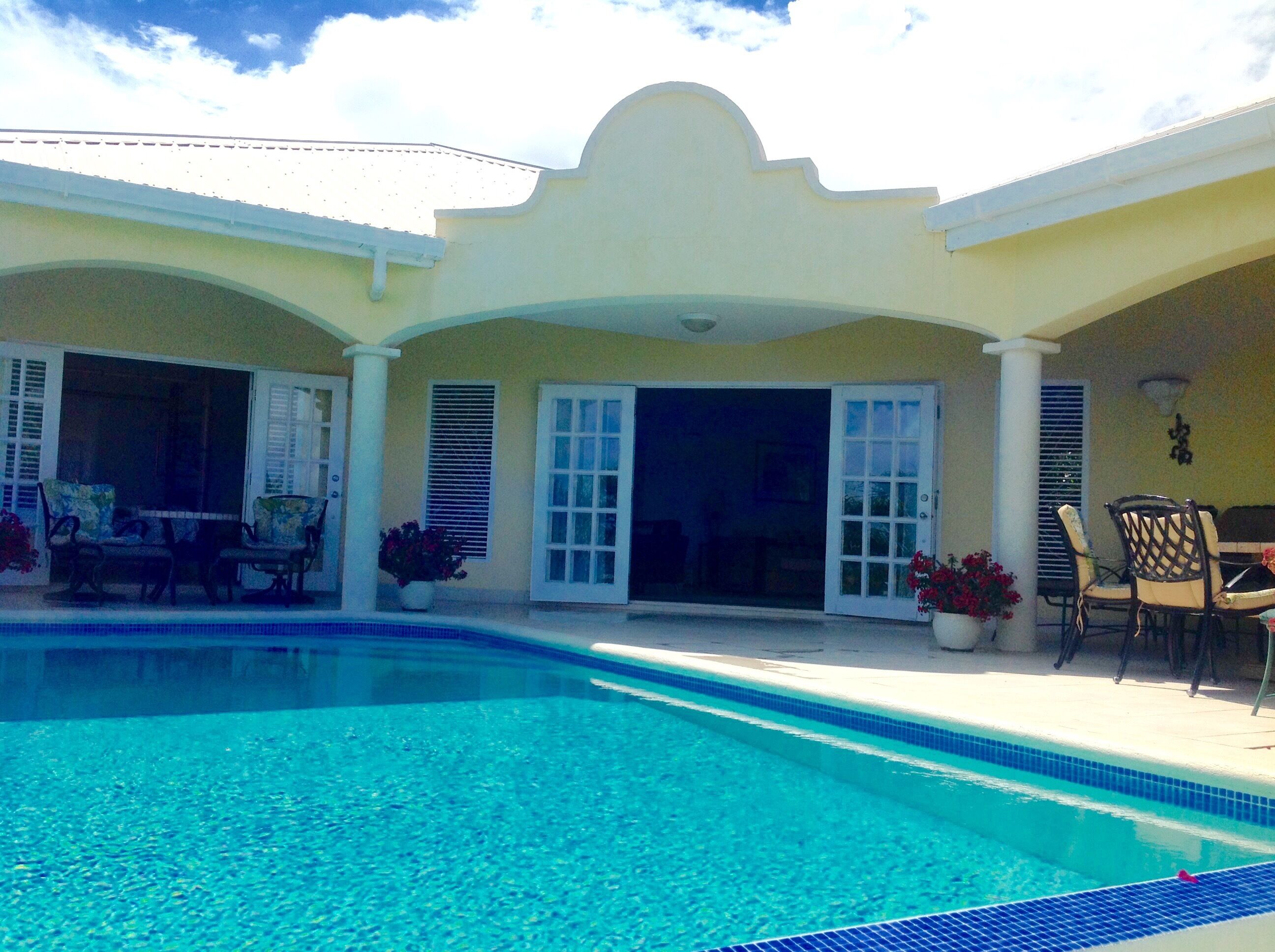 A pool in front of the villa with arches and open glass doors.