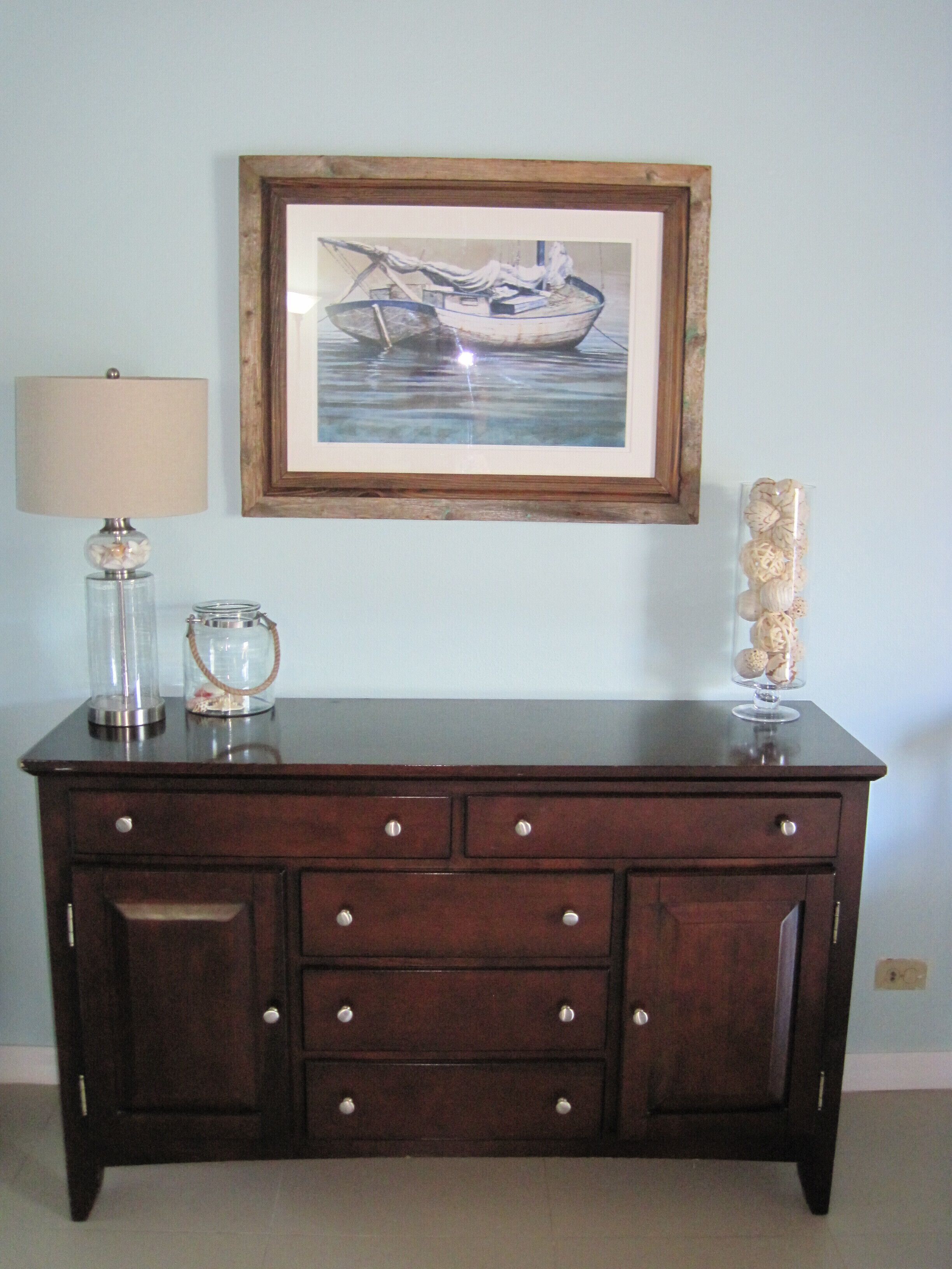 A sideboard with a lamp and a framed boat painting.