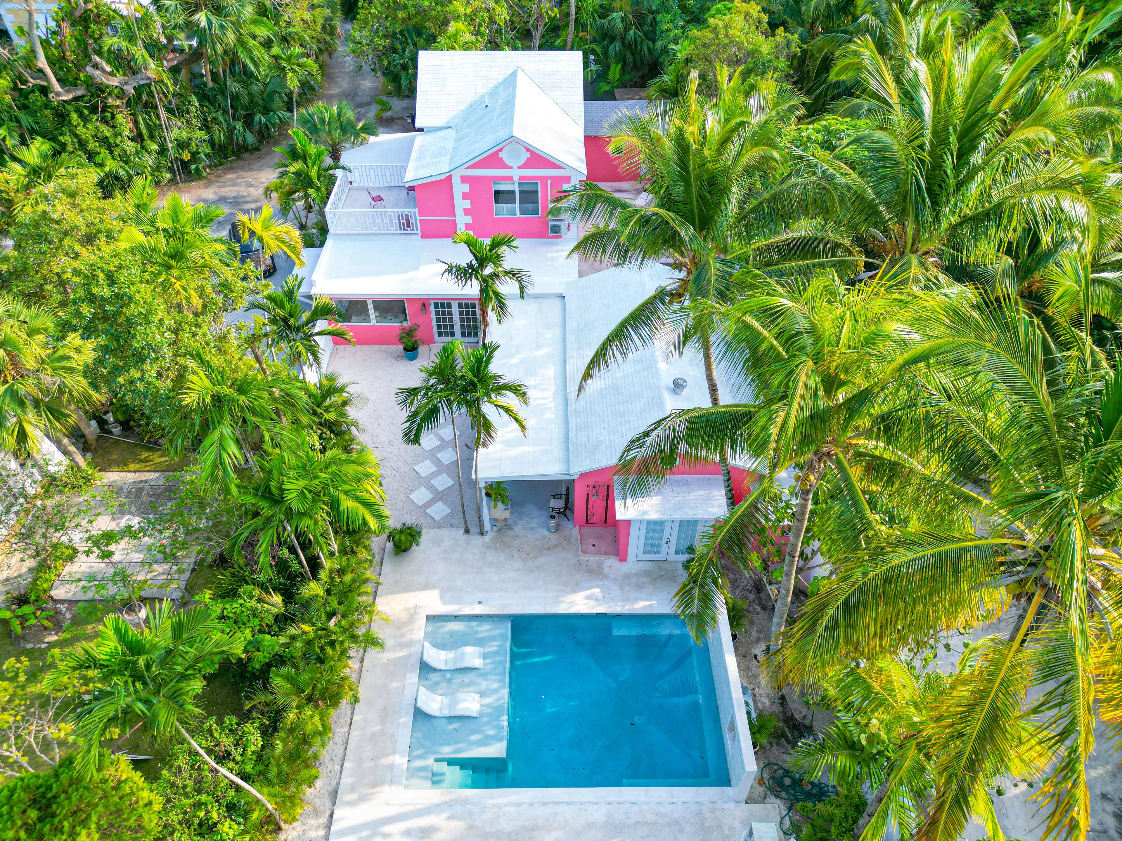 An aerial view of the pink villa, the pool, and the palm trees.