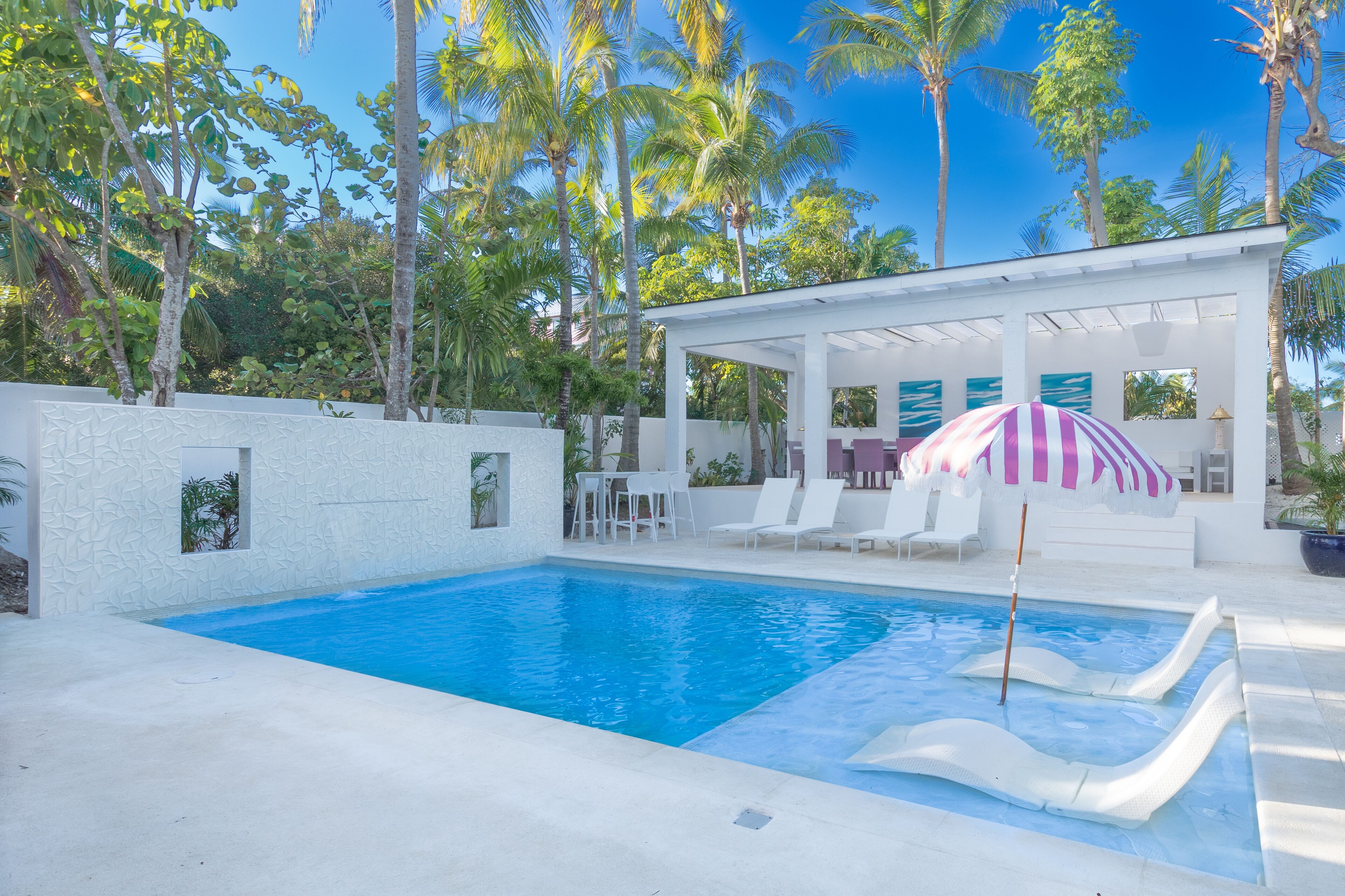 The pool with two sun loungers on the shallow shelf and a striped umbrella.