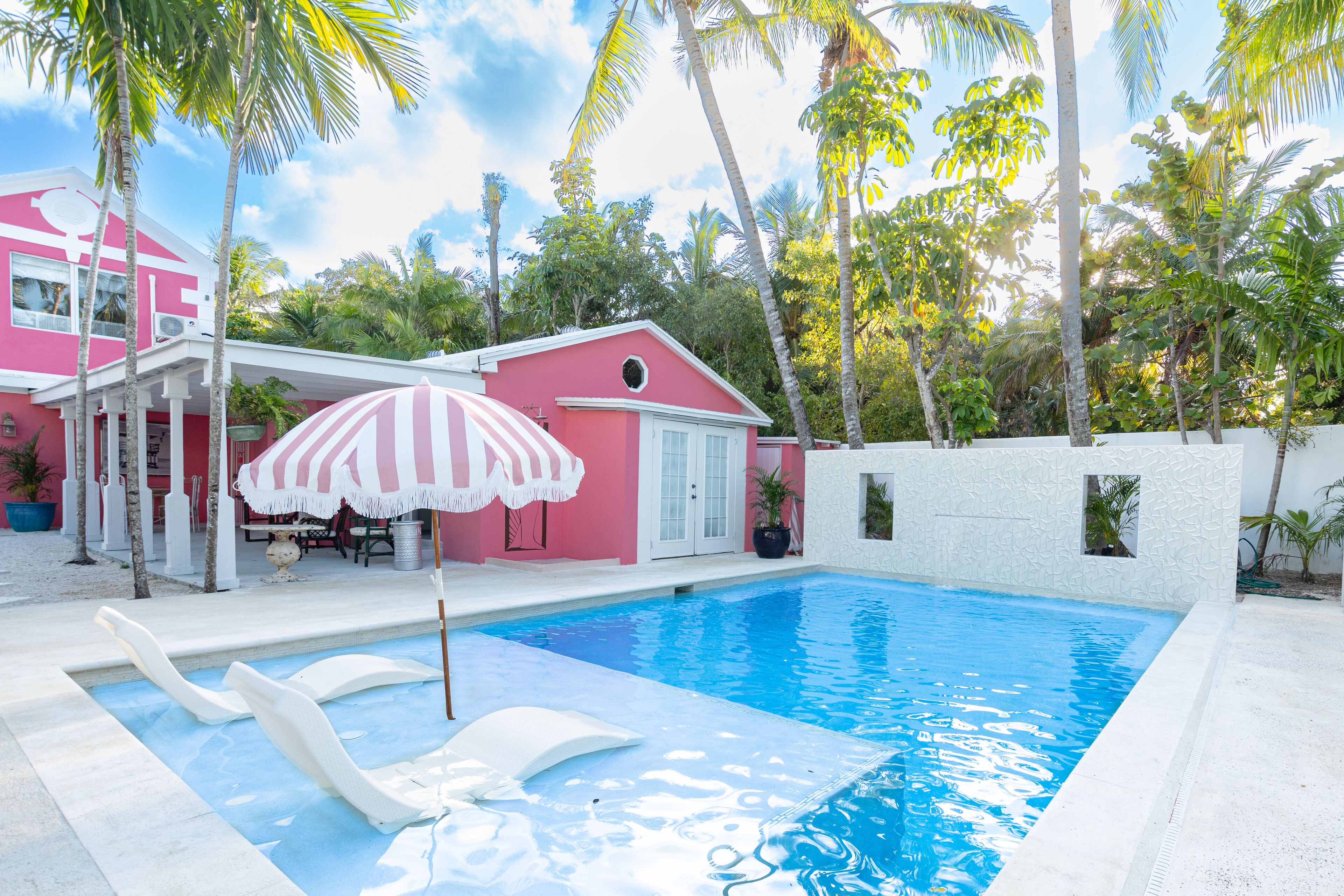 The pool with a striped umbrella in front of the pink villa.
