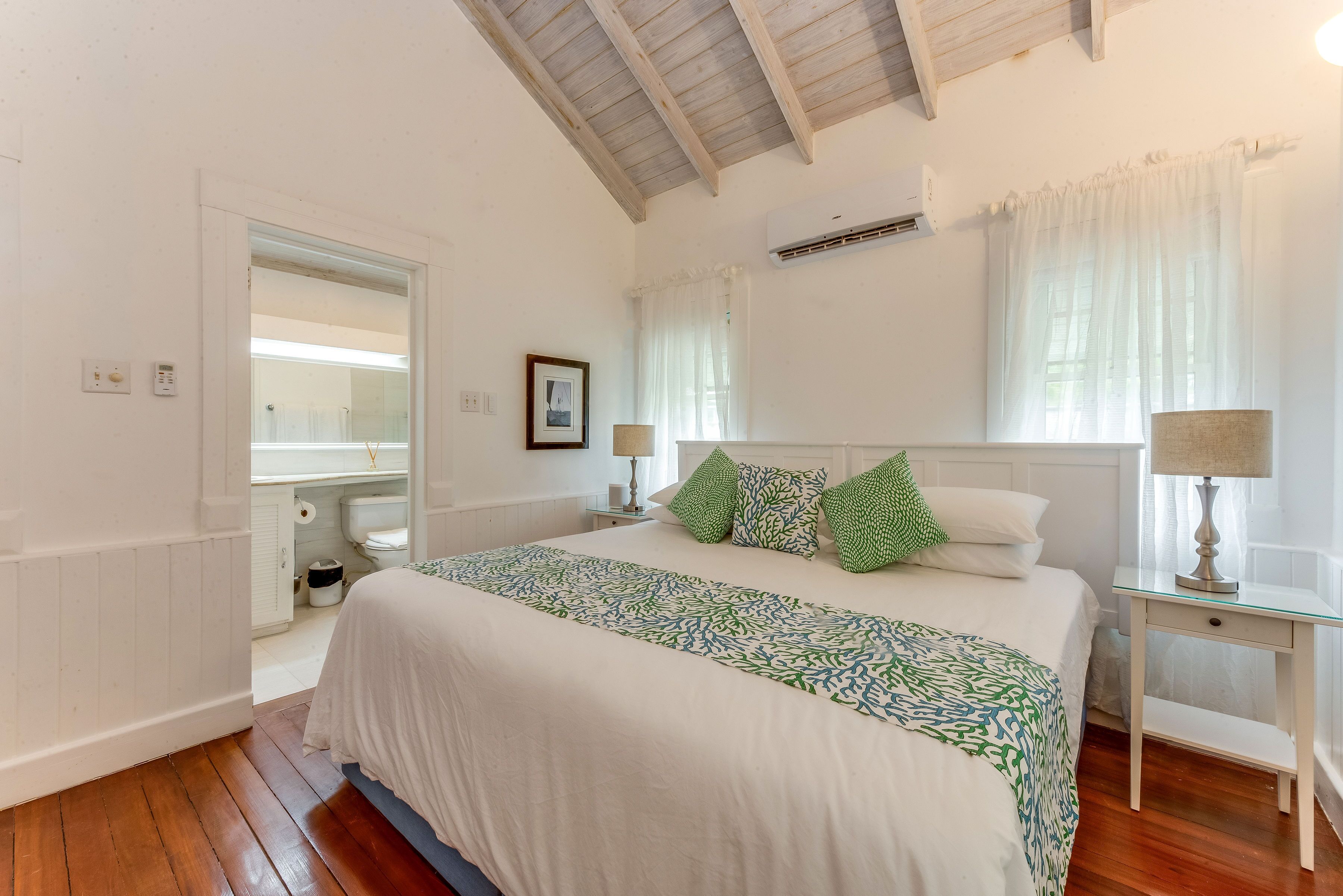 A bedroom with a king bed and green coral-pattern cushions.