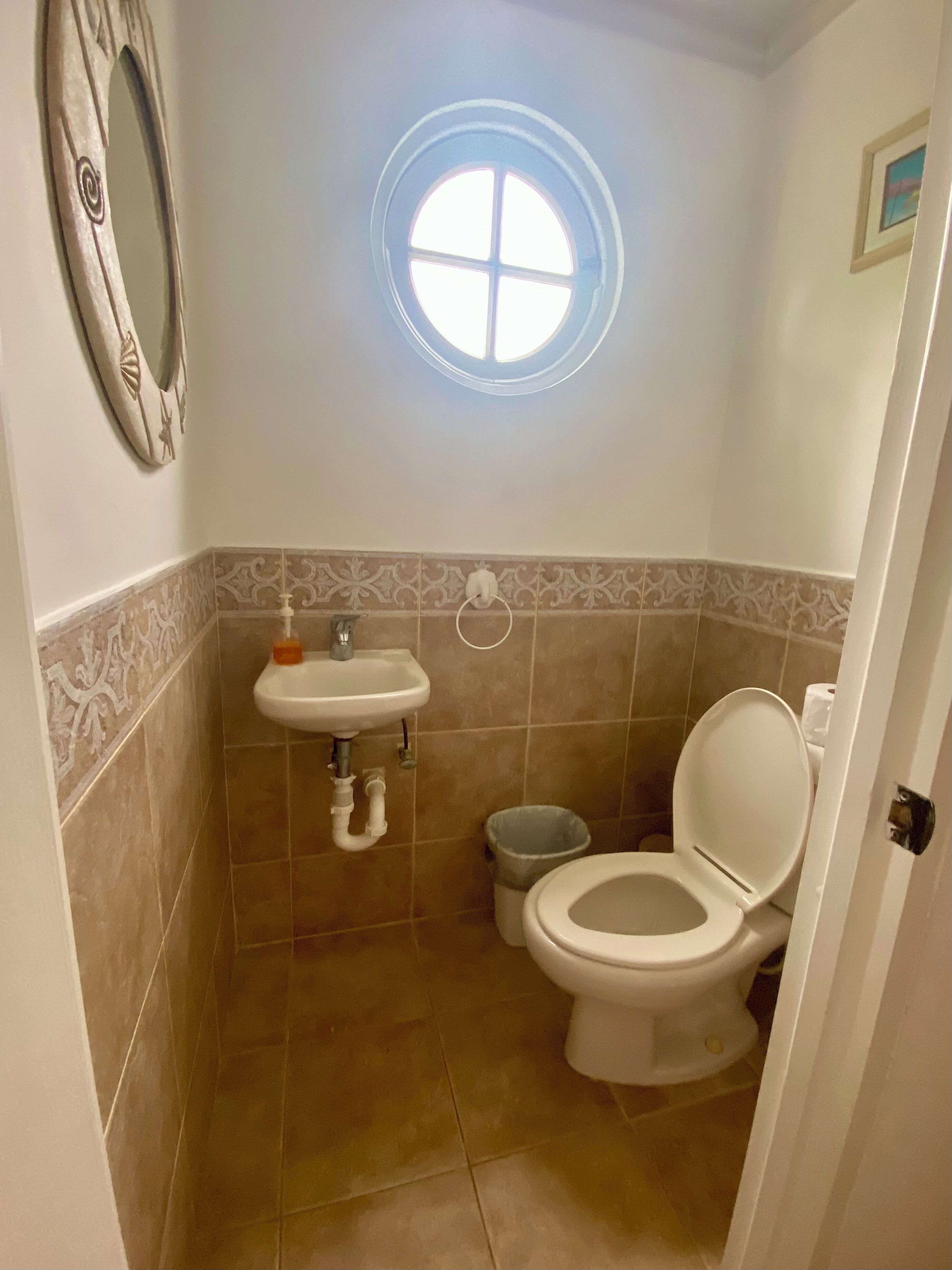 A toilet room with a wall sink and a round window.