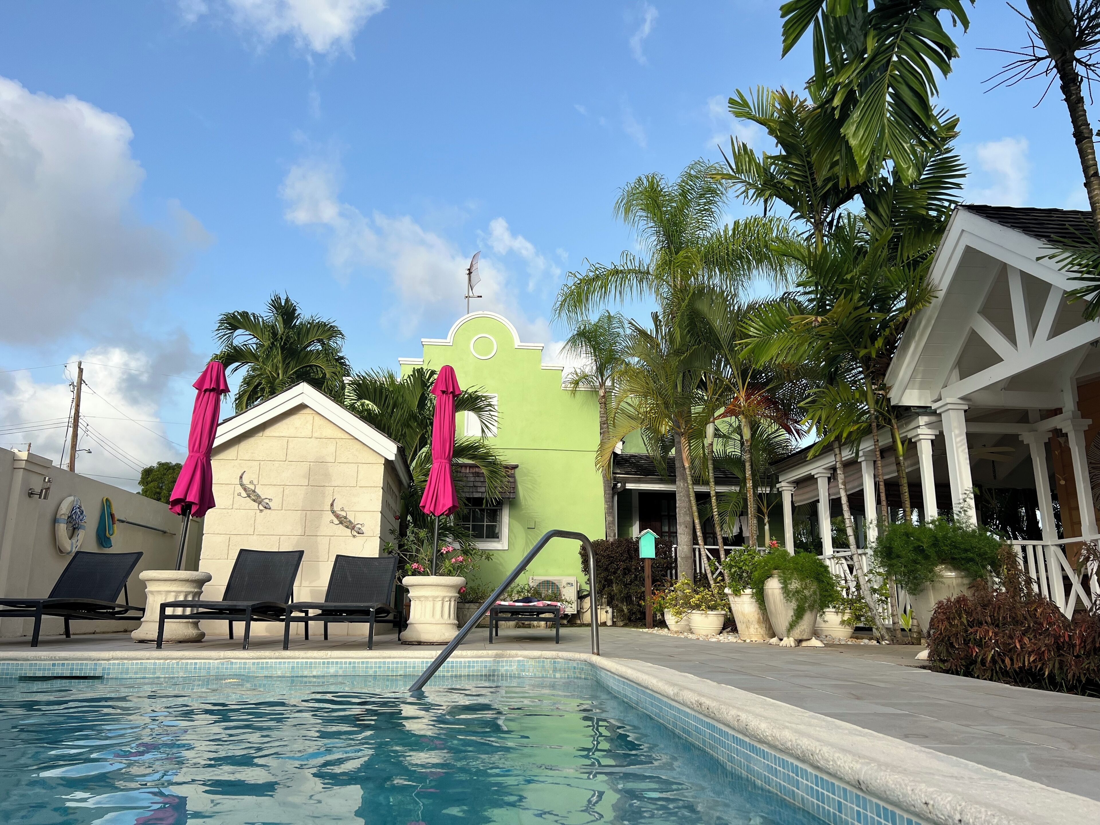 A view of the pool, the loungers, and the green building.