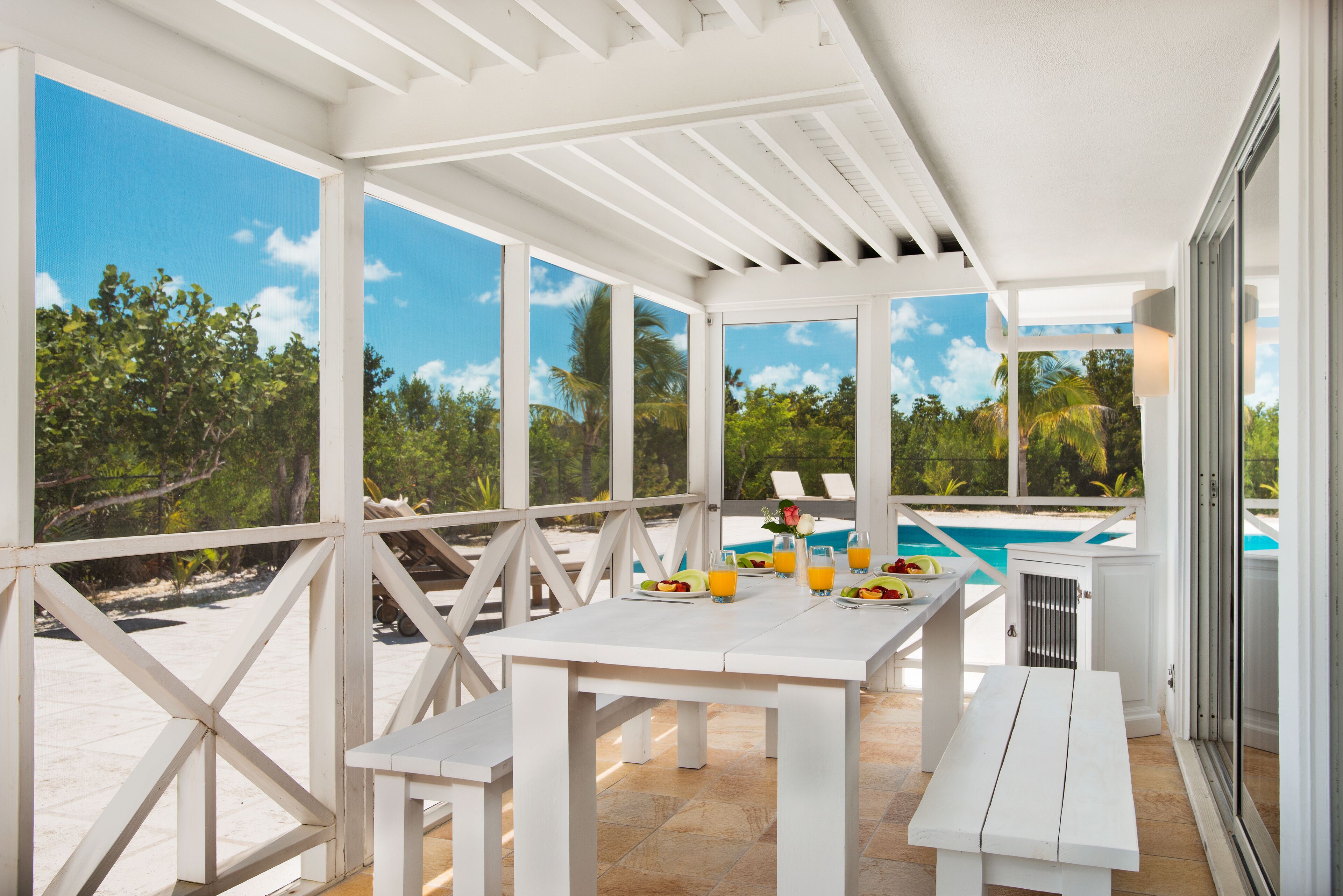 A white table and benches on the screened porch.