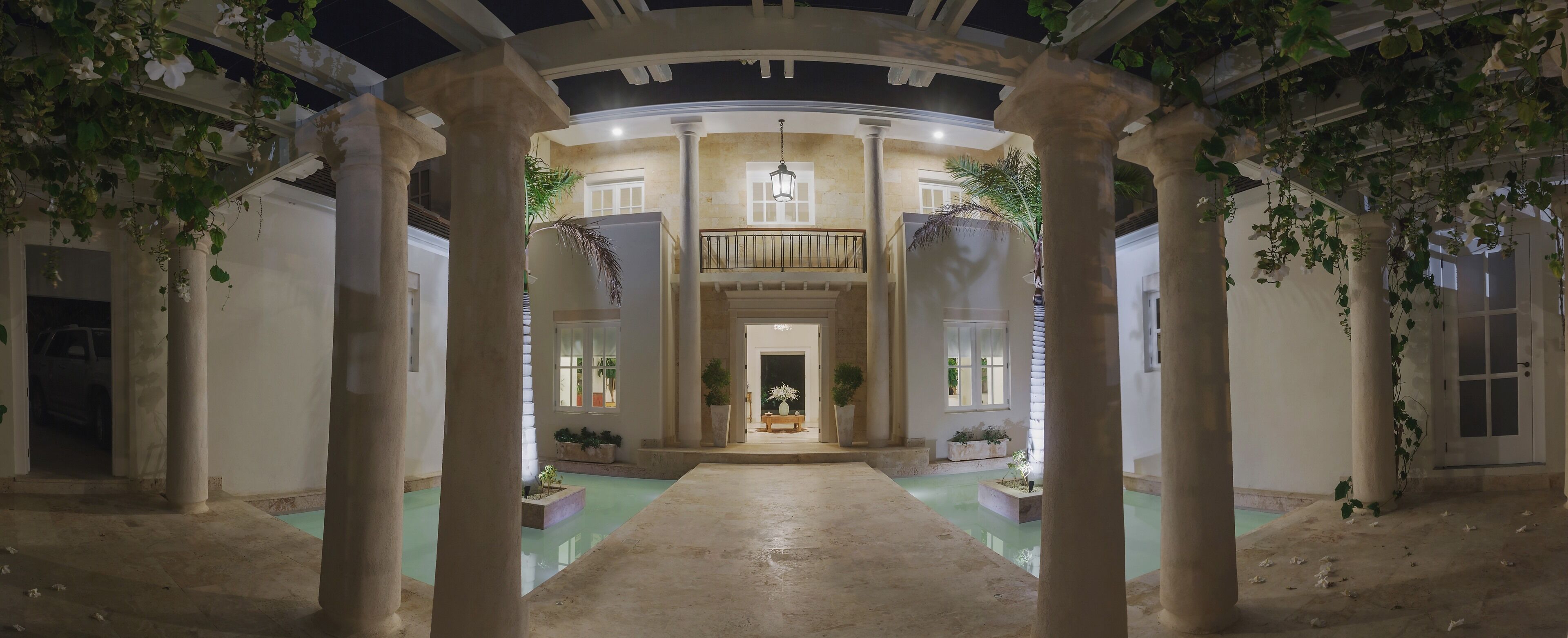 A view of the villa entrance at night between columns and water features.