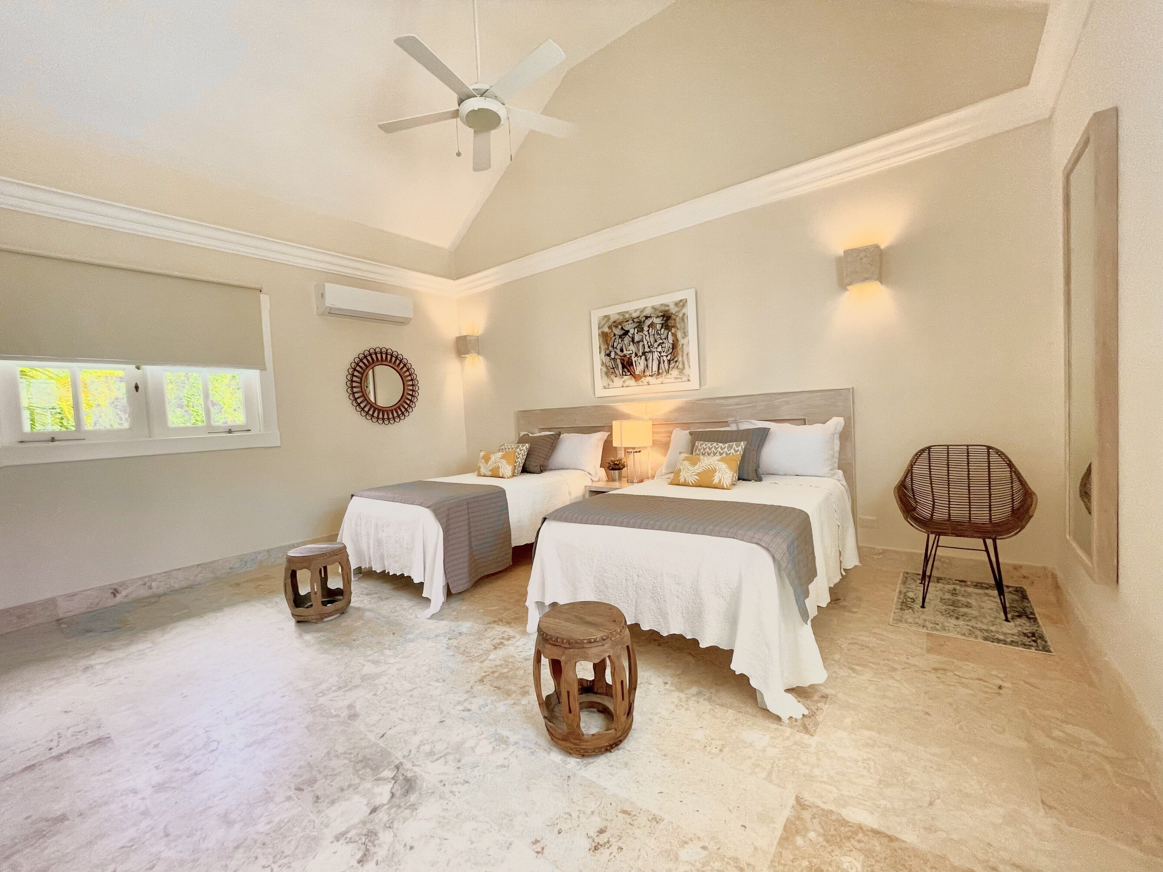 A bedroom with two beds, a ceiling fan, and a rattan chair.