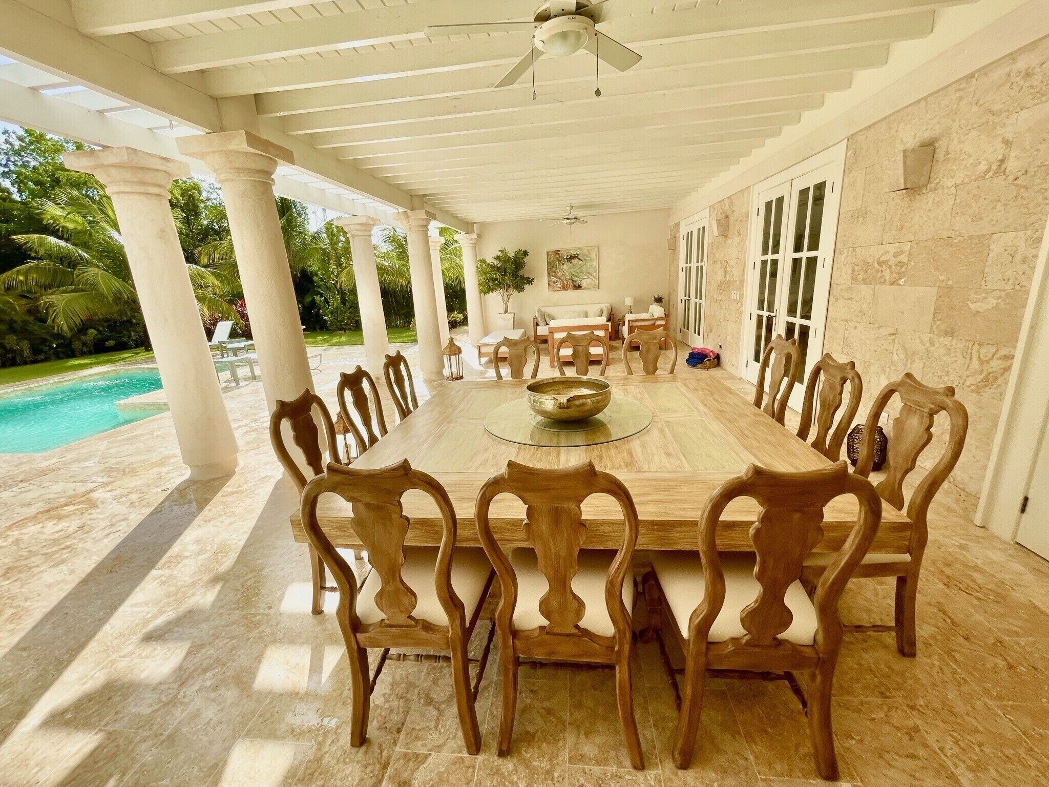 A covered terrace with a large wooden dining table next to the pool.