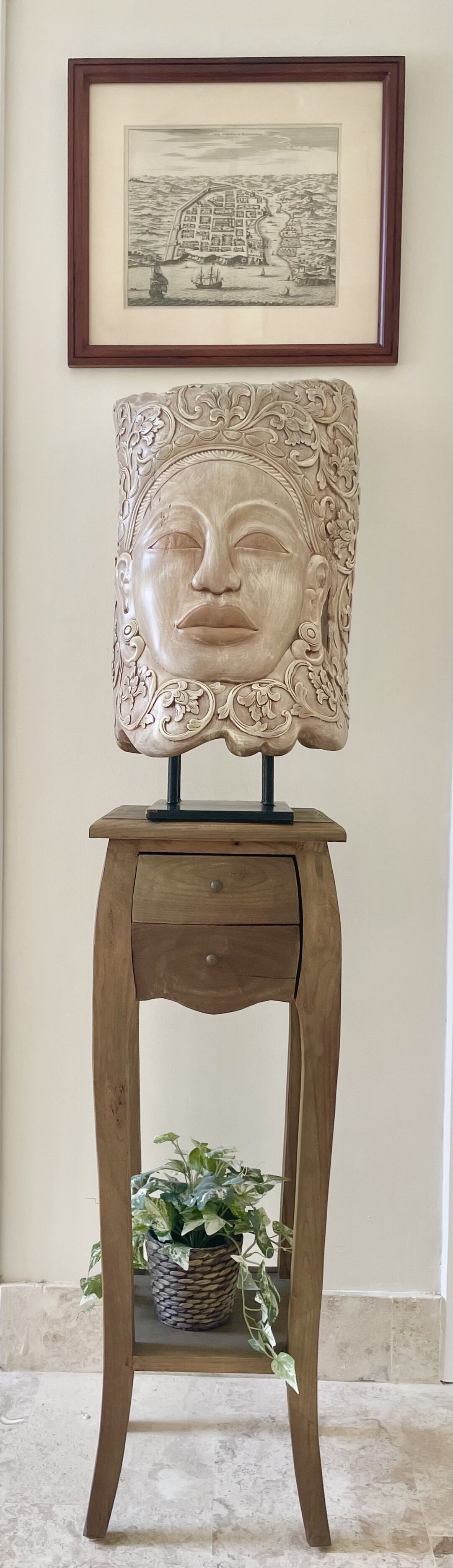 A carved wooden sculpture on a stand, with a framed print above.