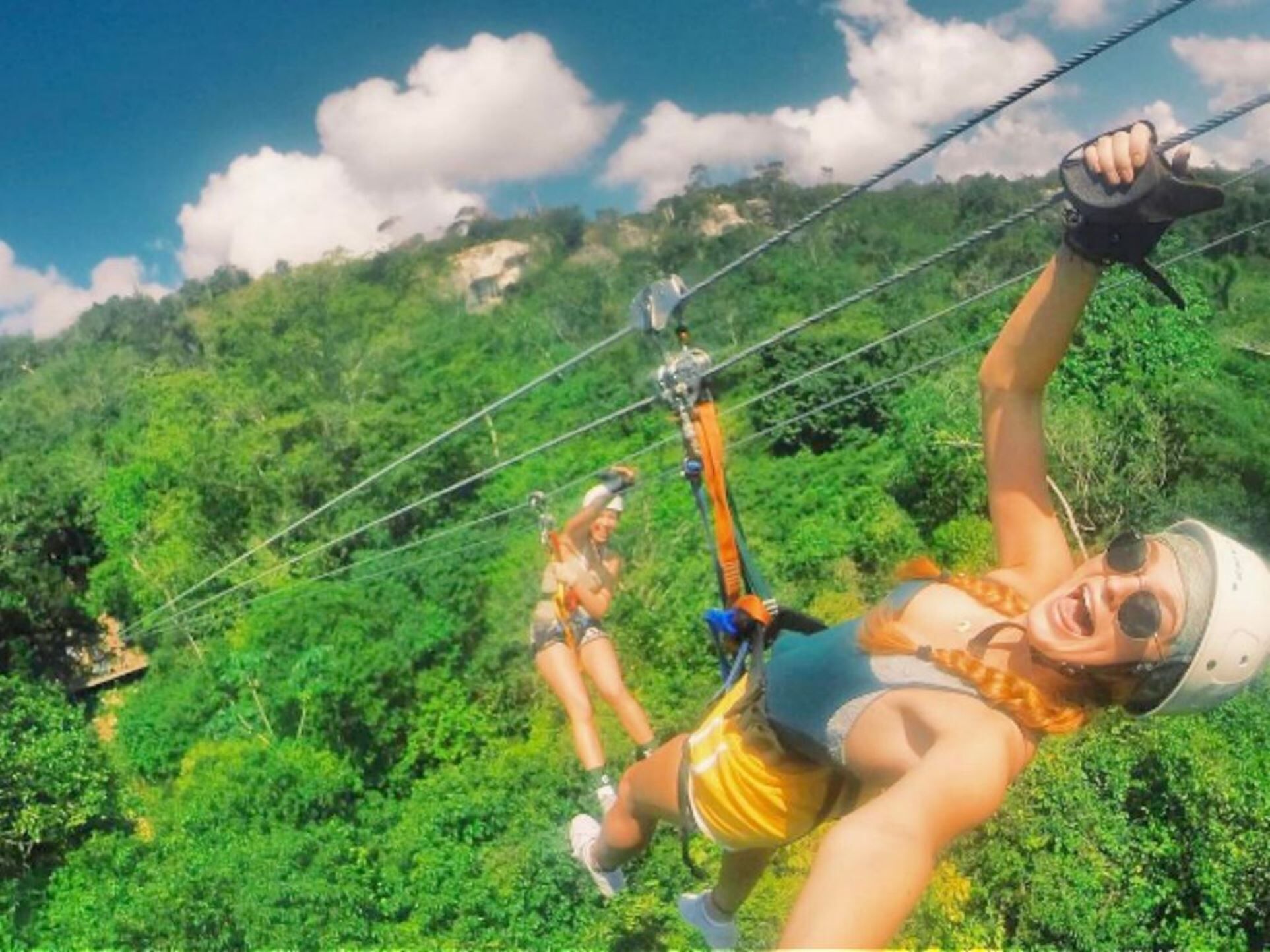 Two persons ride a zipline above the forest.