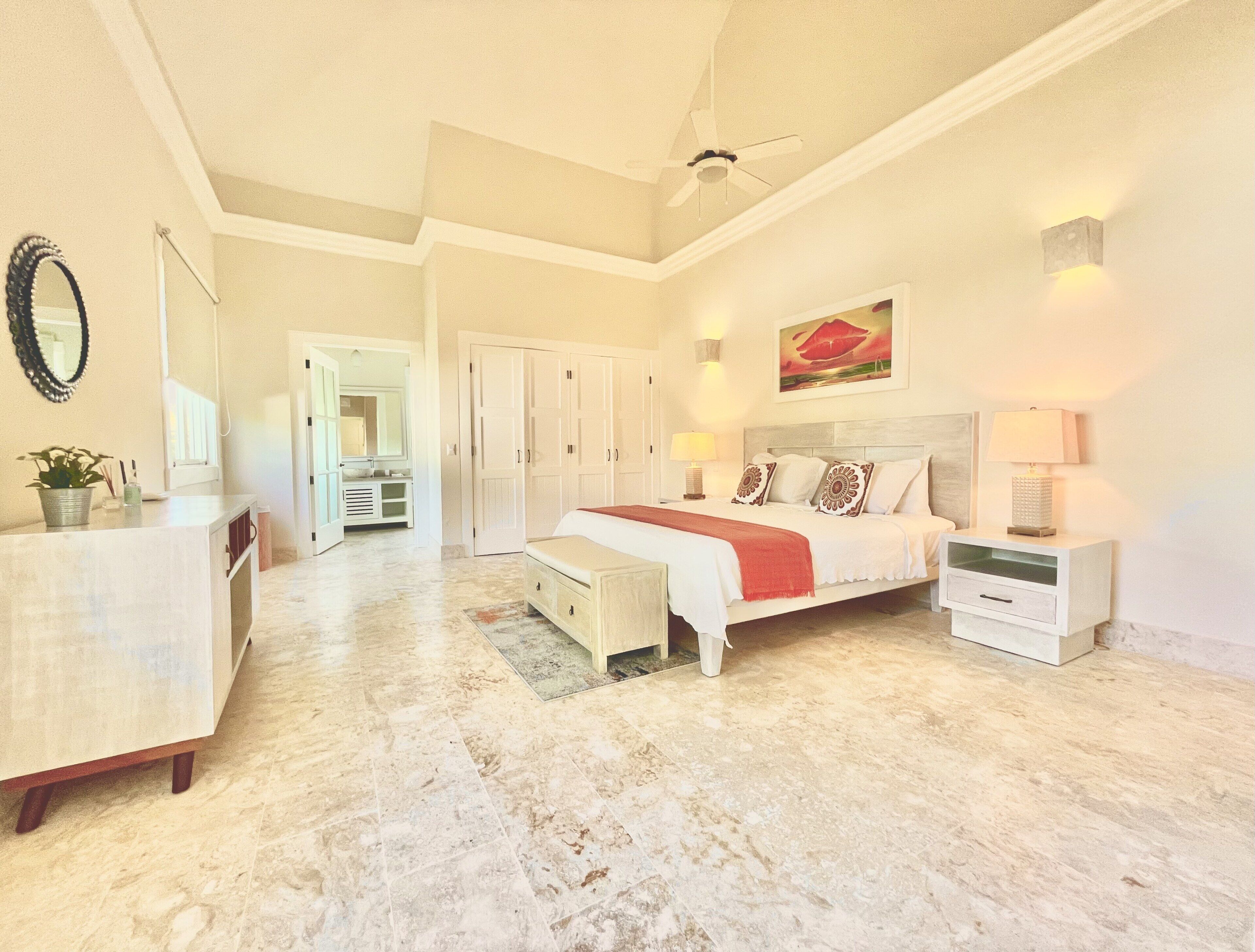 A bedroom with a large bed, a dresser, and a door to the bathroom.