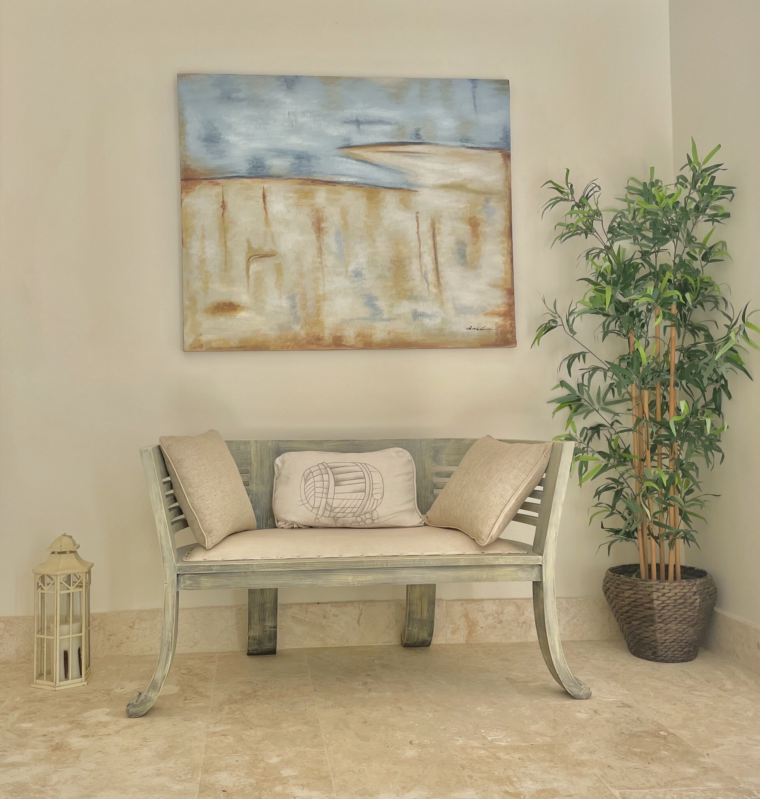 A bench with cushions below an abstract painting, next to a plant.