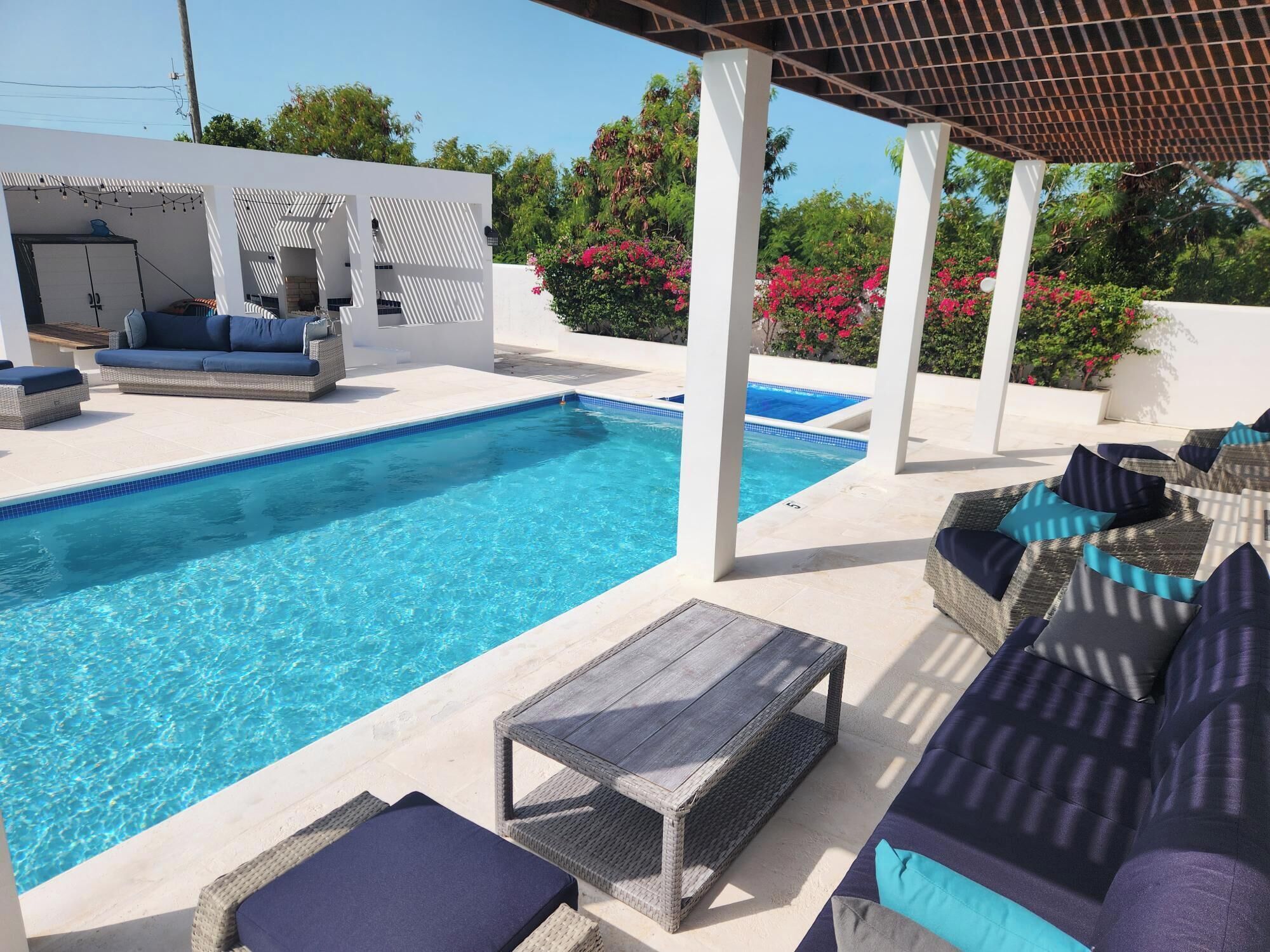 Sofas under the pergola at the side of the pool.