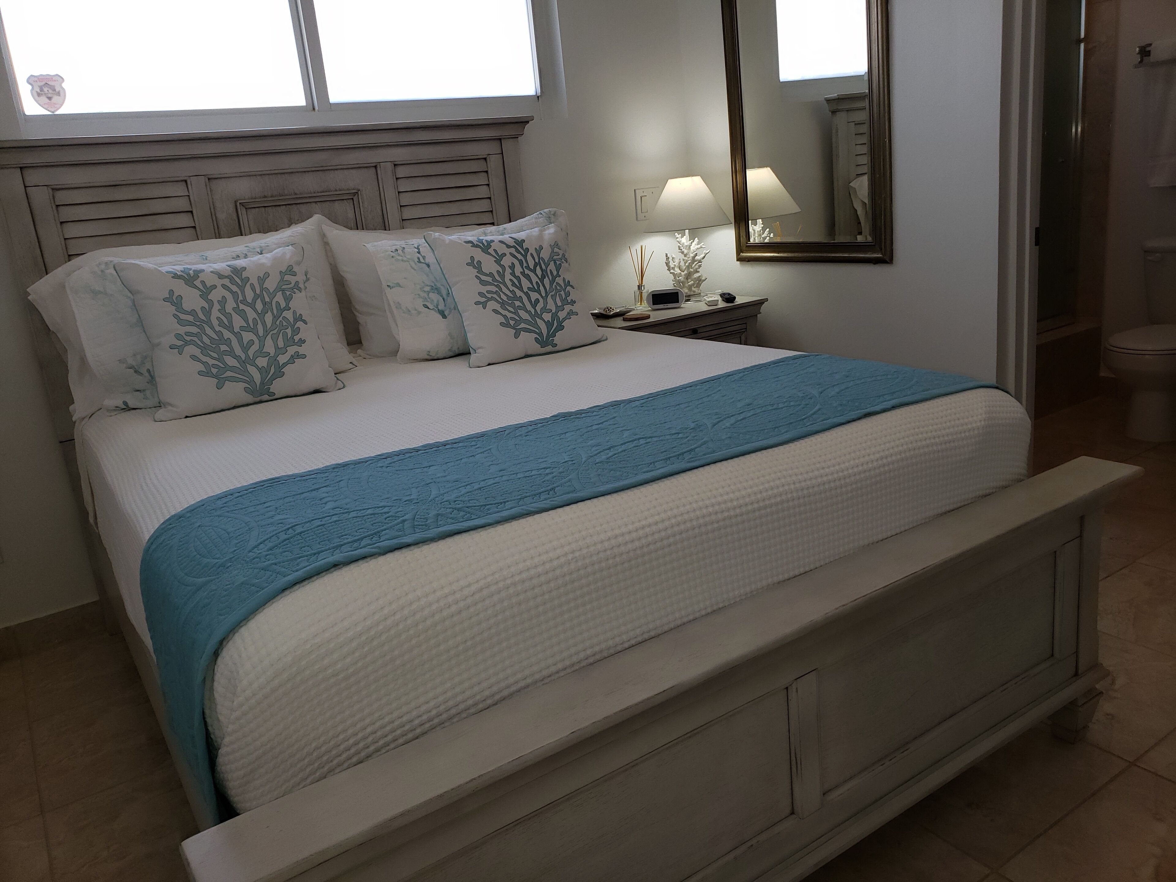 A bedroom with a gray wood bed and coral pattern pillows.