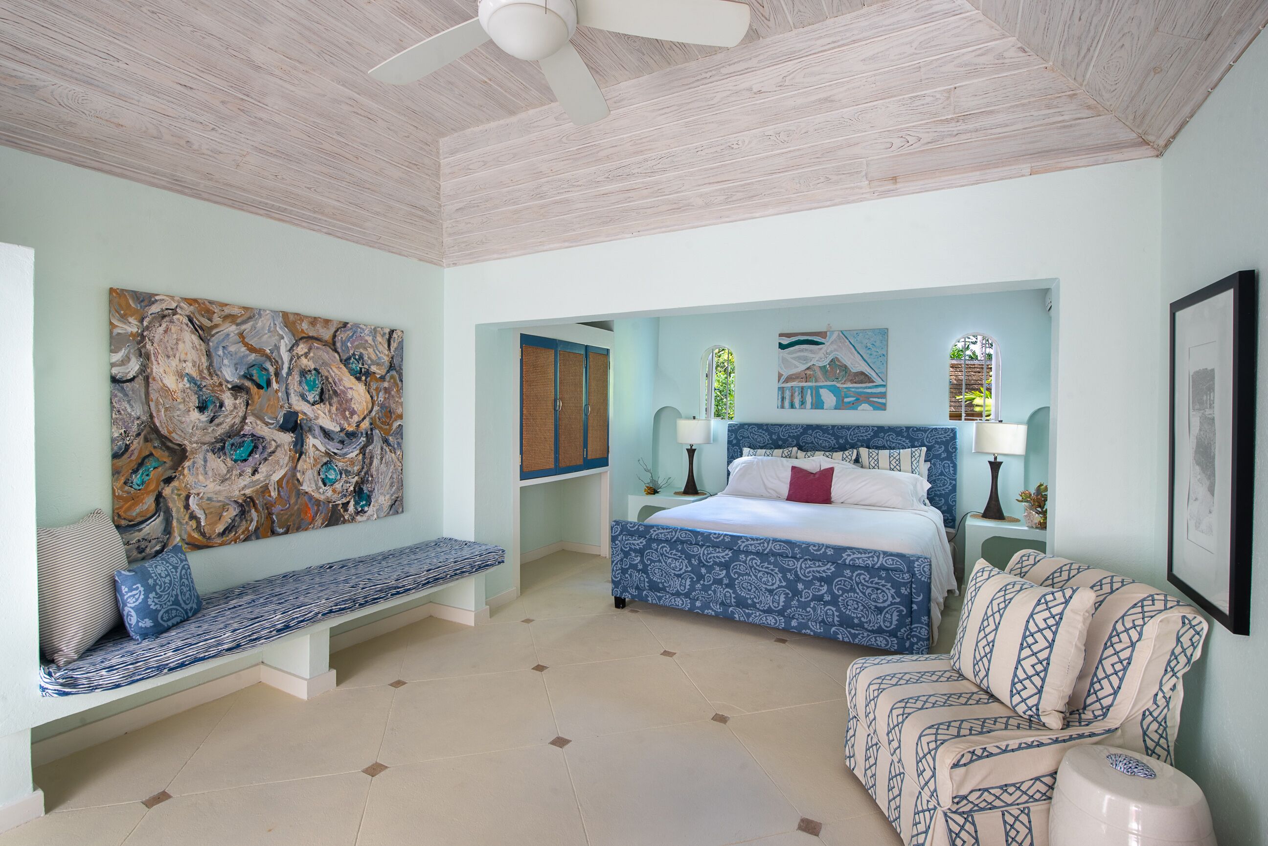 A bedroom with a blue upholstered bed, a wall bench, and a large painting.