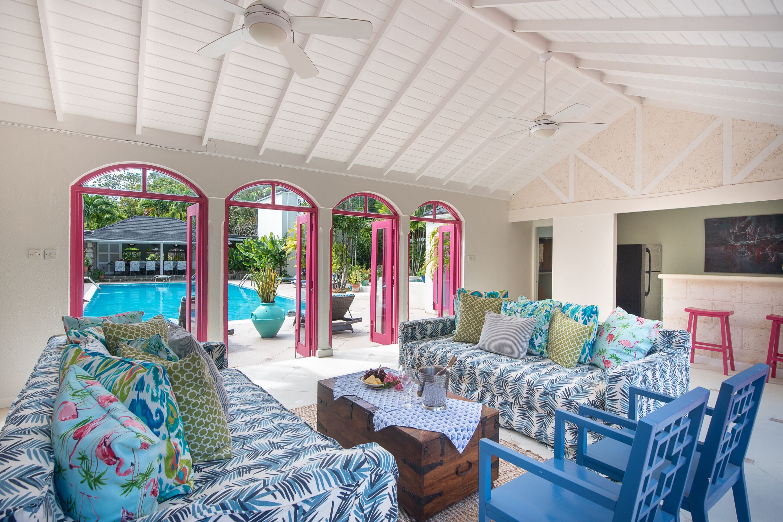 A covered lounge with two sofas and pink arched doors that open to the pool.