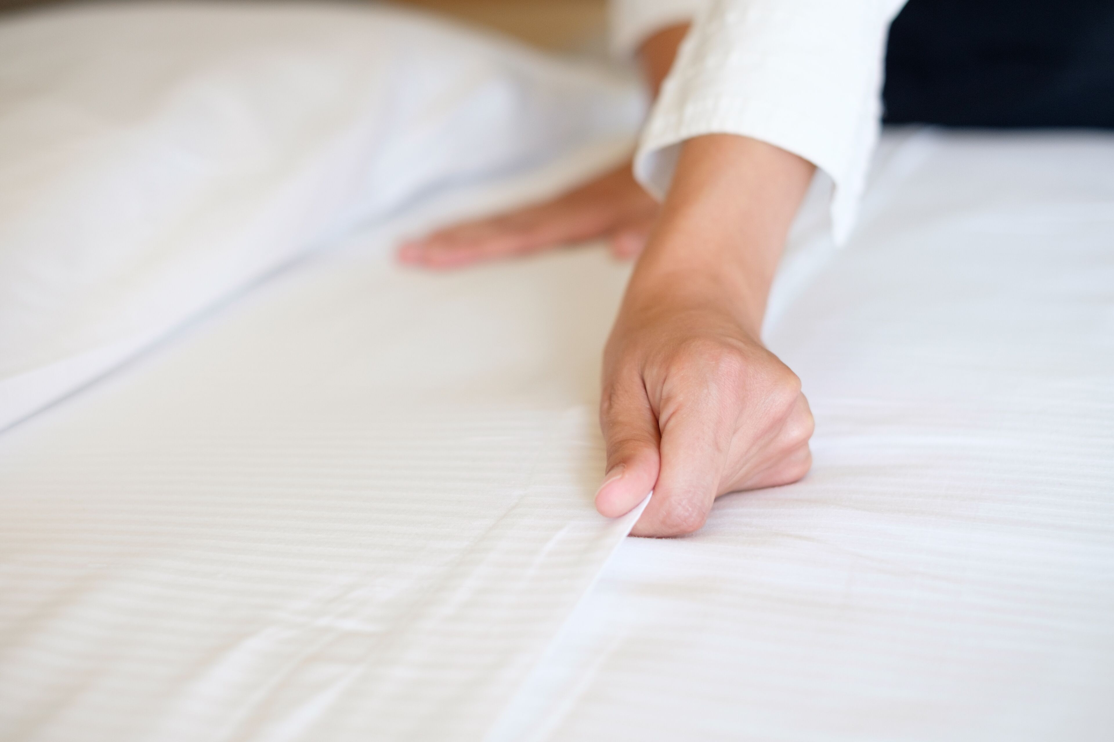 A person smooths a white sheet on a bed.