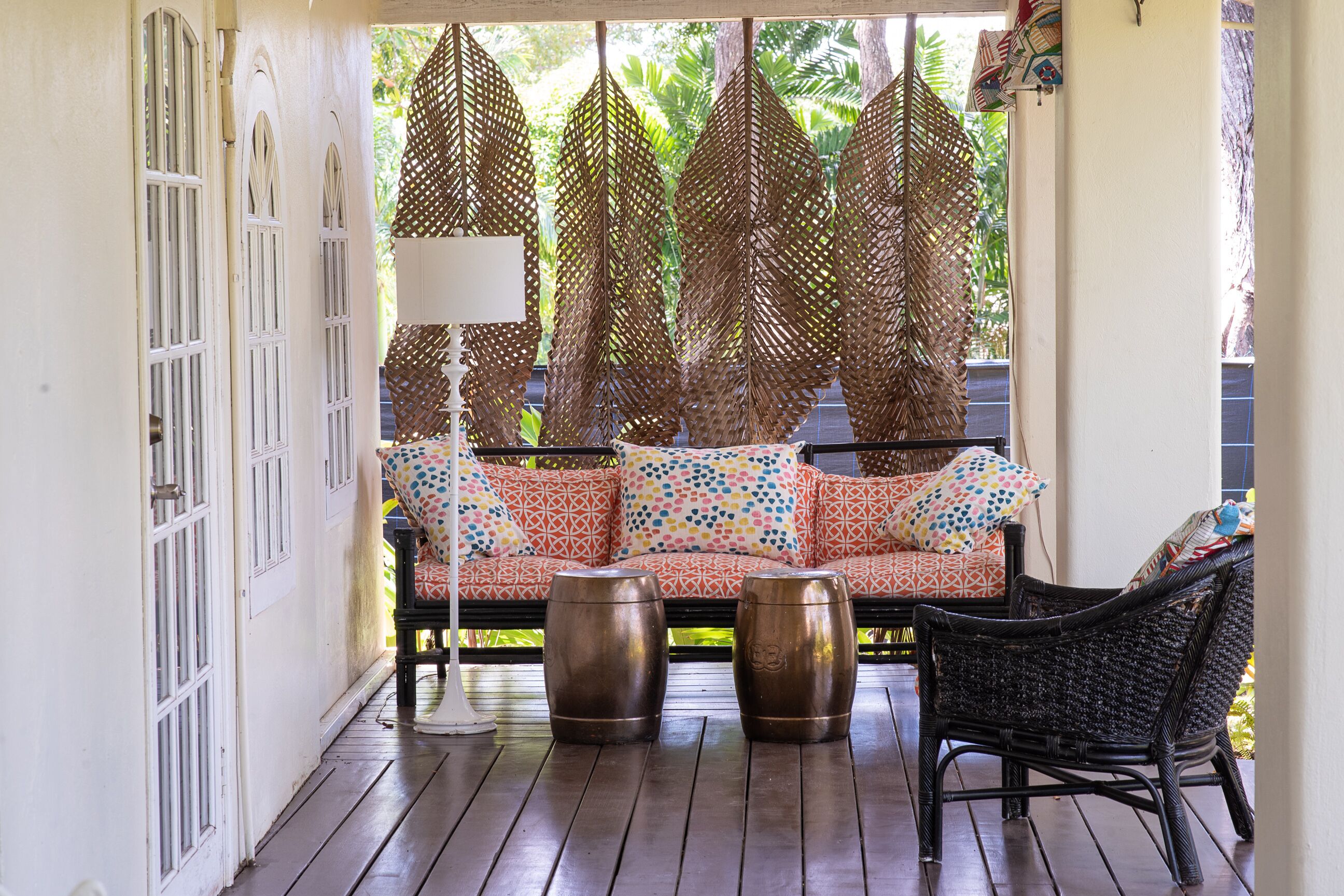 A porch with a sofa, two drum tables, and woven leaf screens.