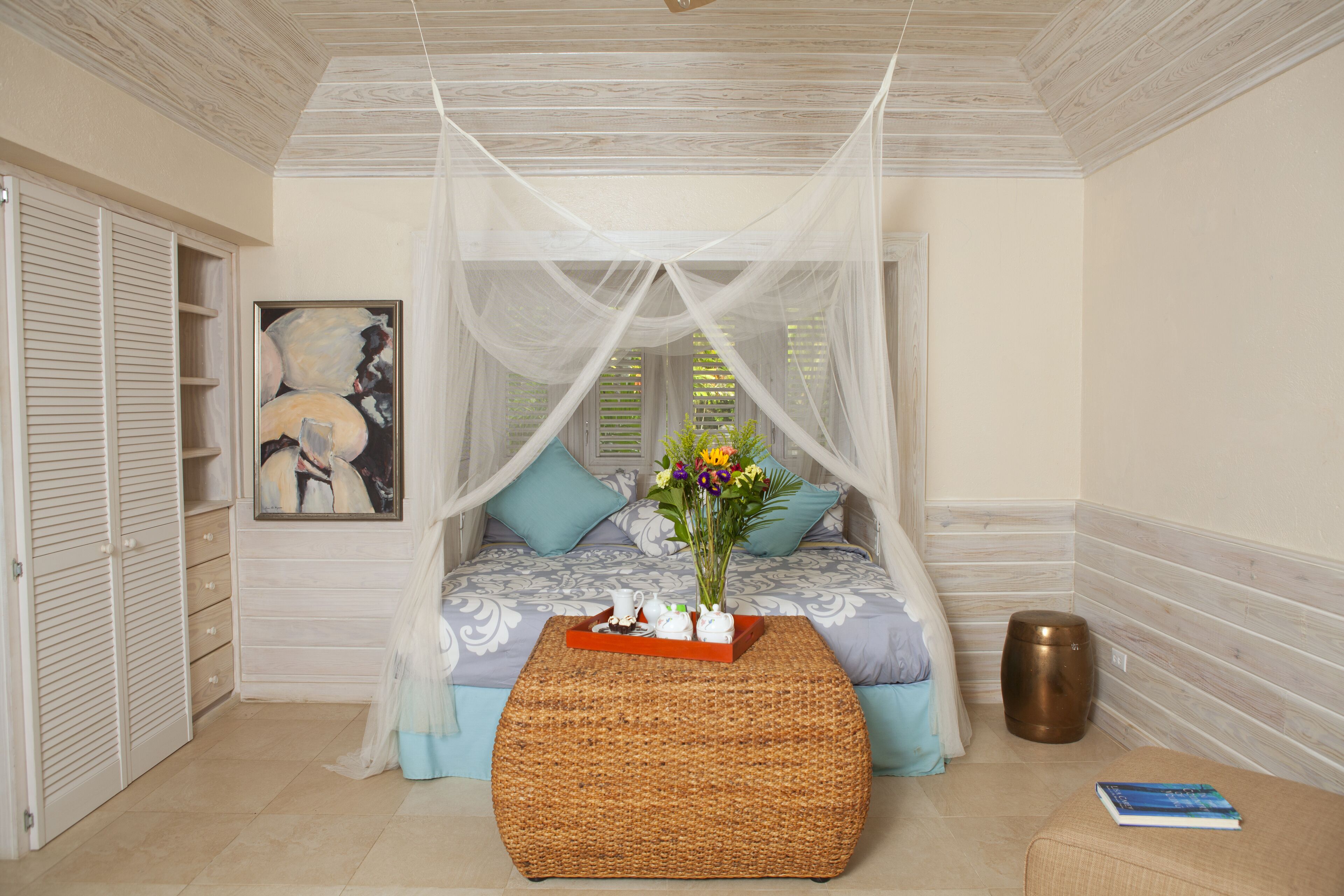 A bedroom with a net canopy over the bed and a wicker table.