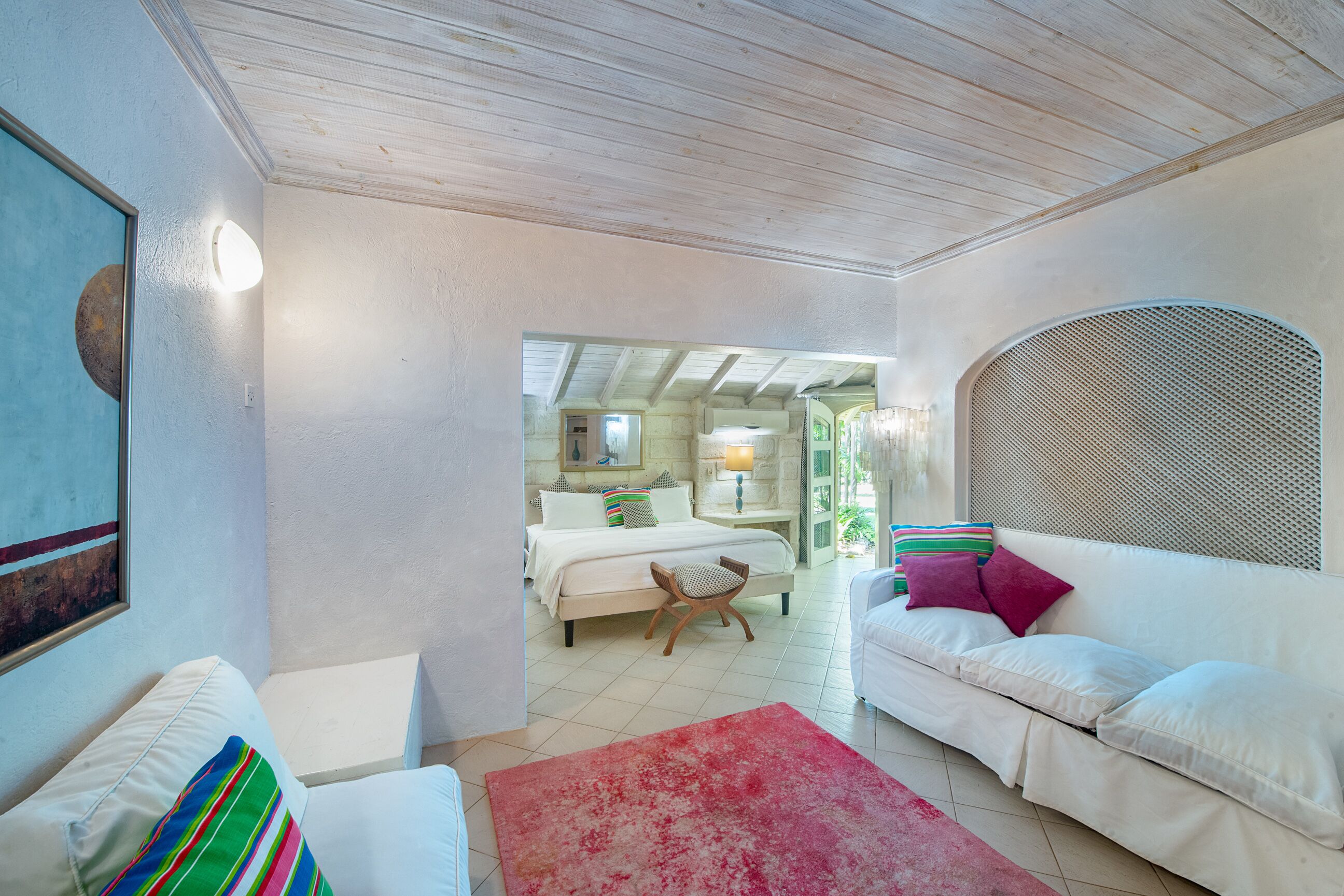 A sitting room with two white sofas next to a bedroom.