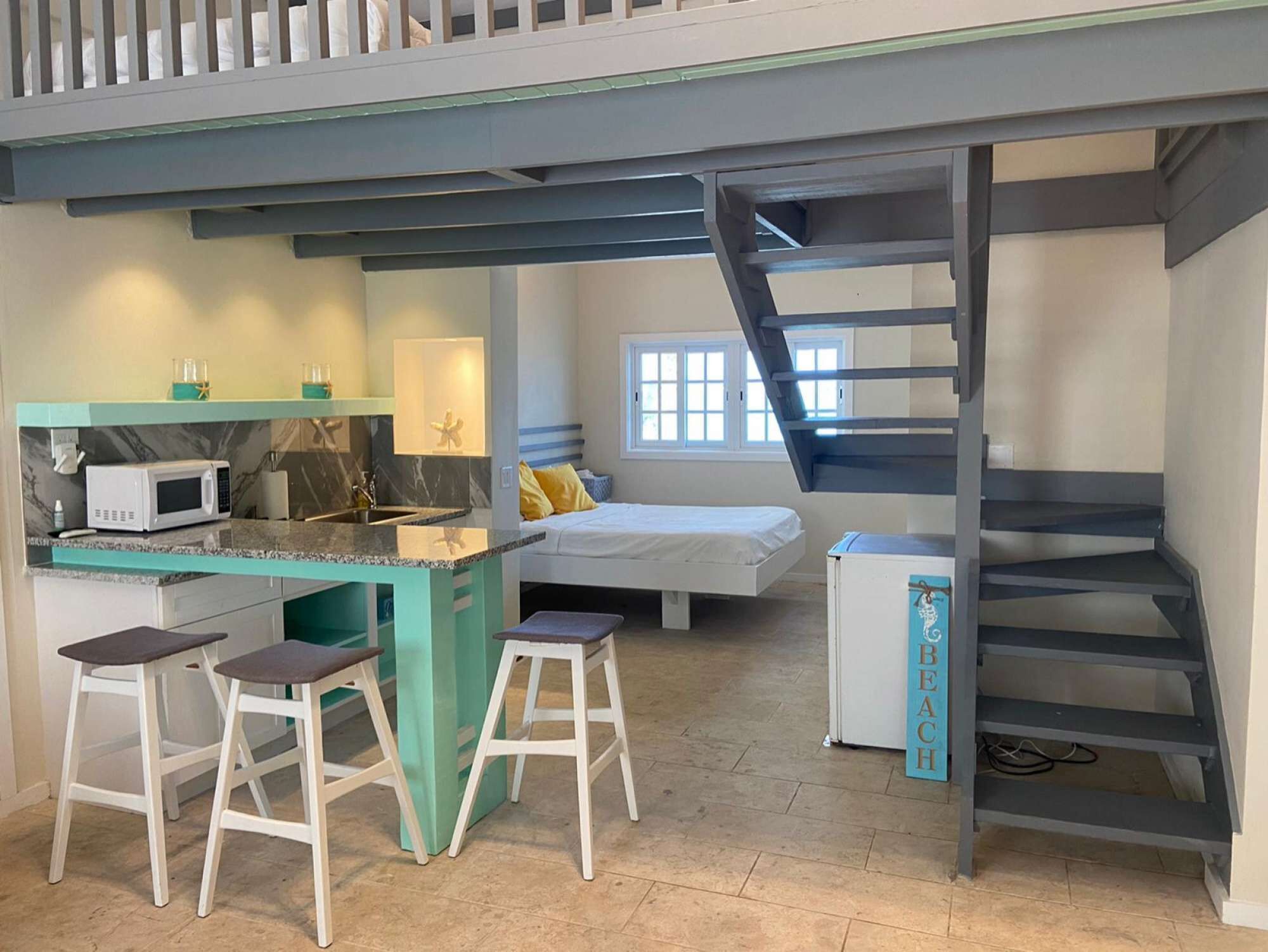 A studio room with a small kitchen, a bed, and stairs to a loft.