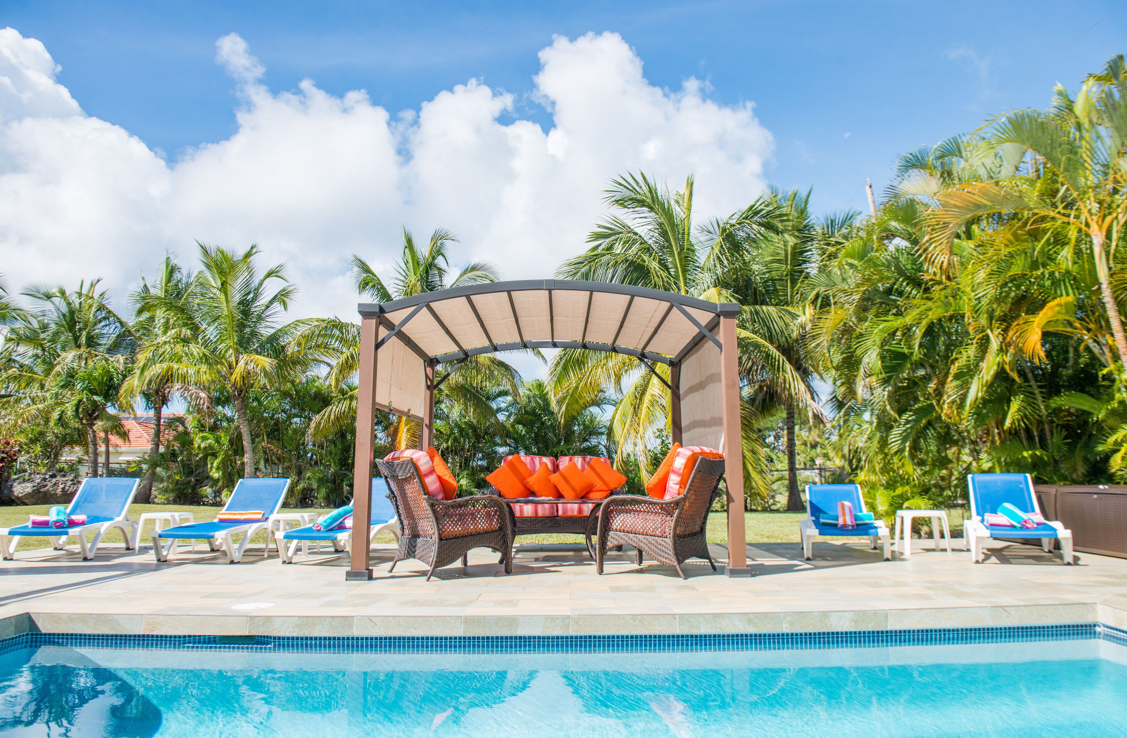 A shade canopy with seats and sun loungers stands at the edge of the pool.