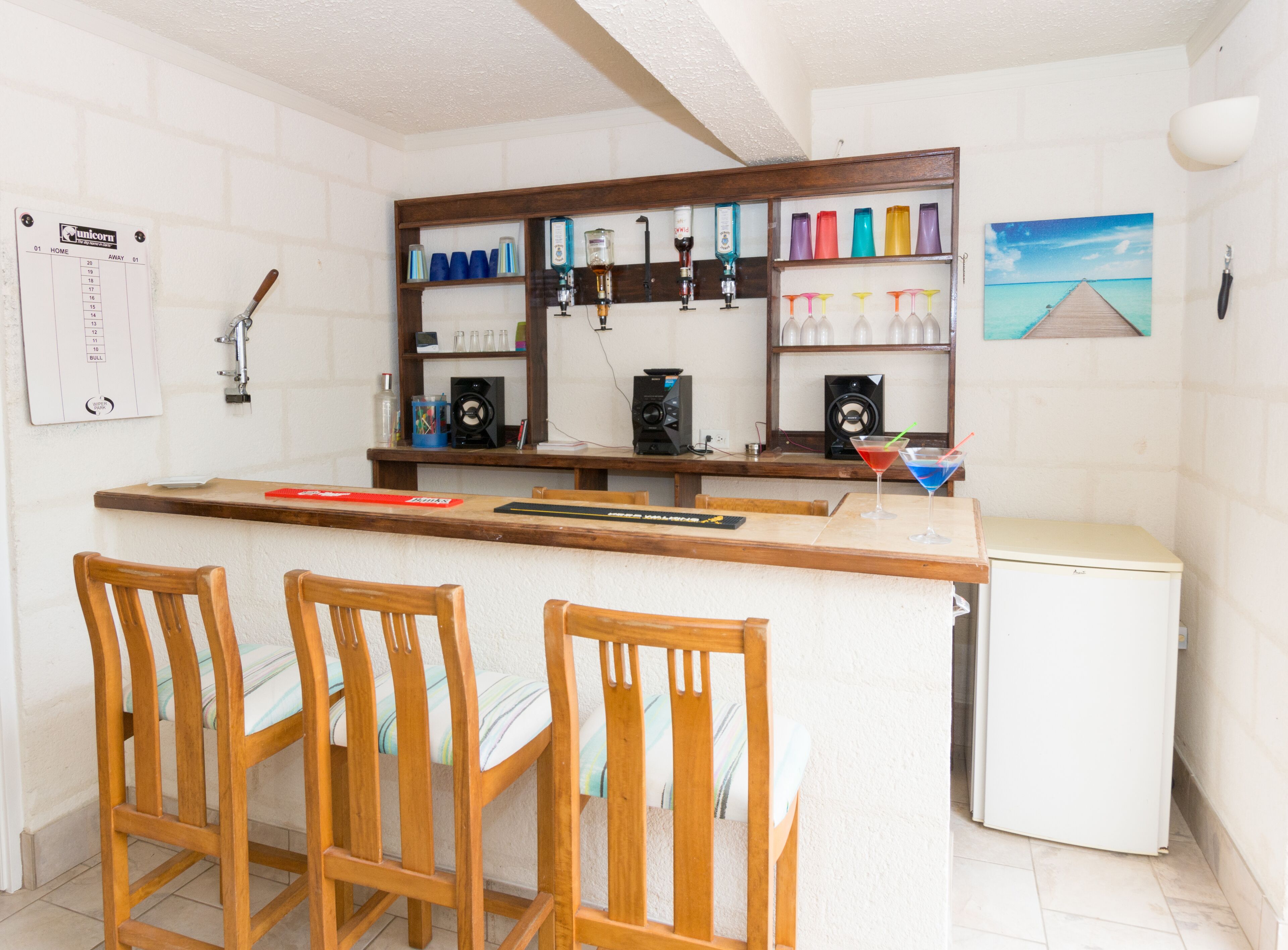 The bar has a stone counter, three stools, and shelves with glasses and bottles.