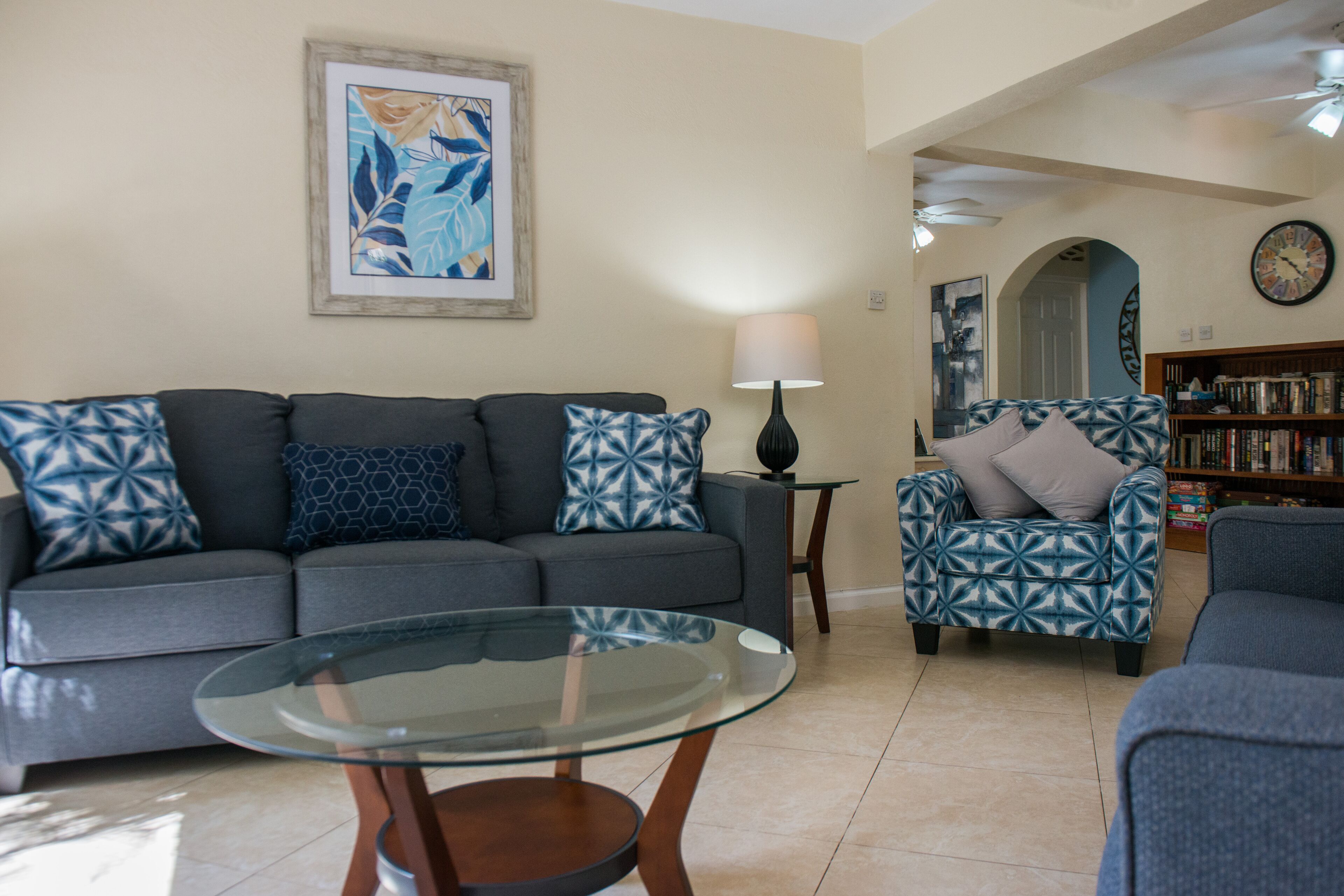 The living room has a gray sofa, two patterned chairs, and a glass coffee table.